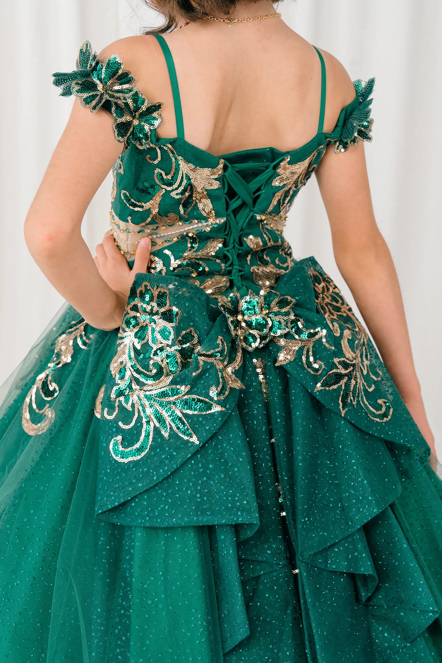 Back close up view of Hunter green mini quince ball gown with off shoulder floral embroidered bodice, glitter tulle skirt, lace up back, and layered bow