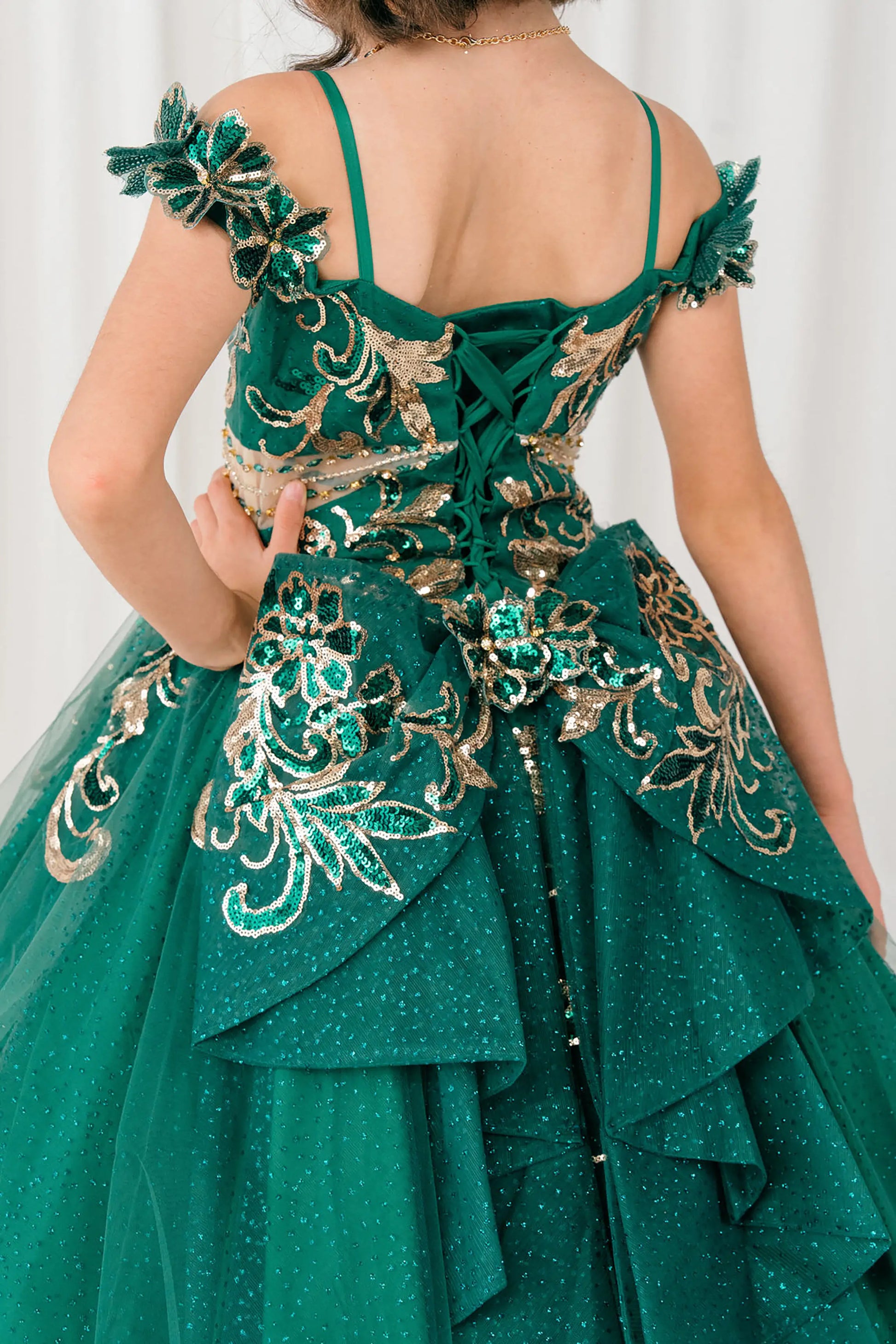 Back close up view of Hunter green mini quince ball gown with off shoulder floral embroidered bodice, glitter tulle skirt, lace up back, and layered bow