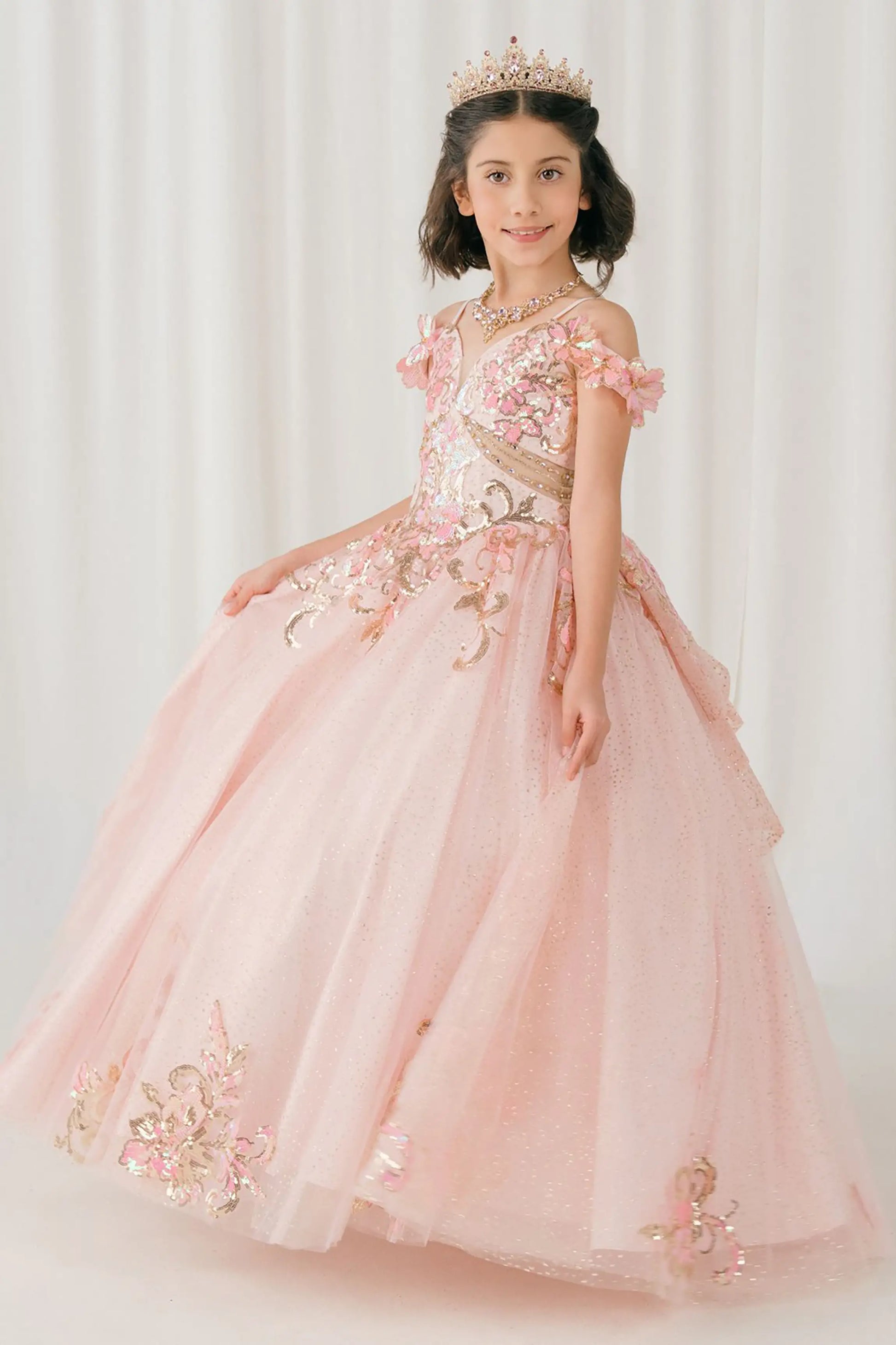 Side full-length view of Pink mini quince ball gown with off shoulder floral embroidered bodice, glitter tulle skirt, lace up back, and layered bow
