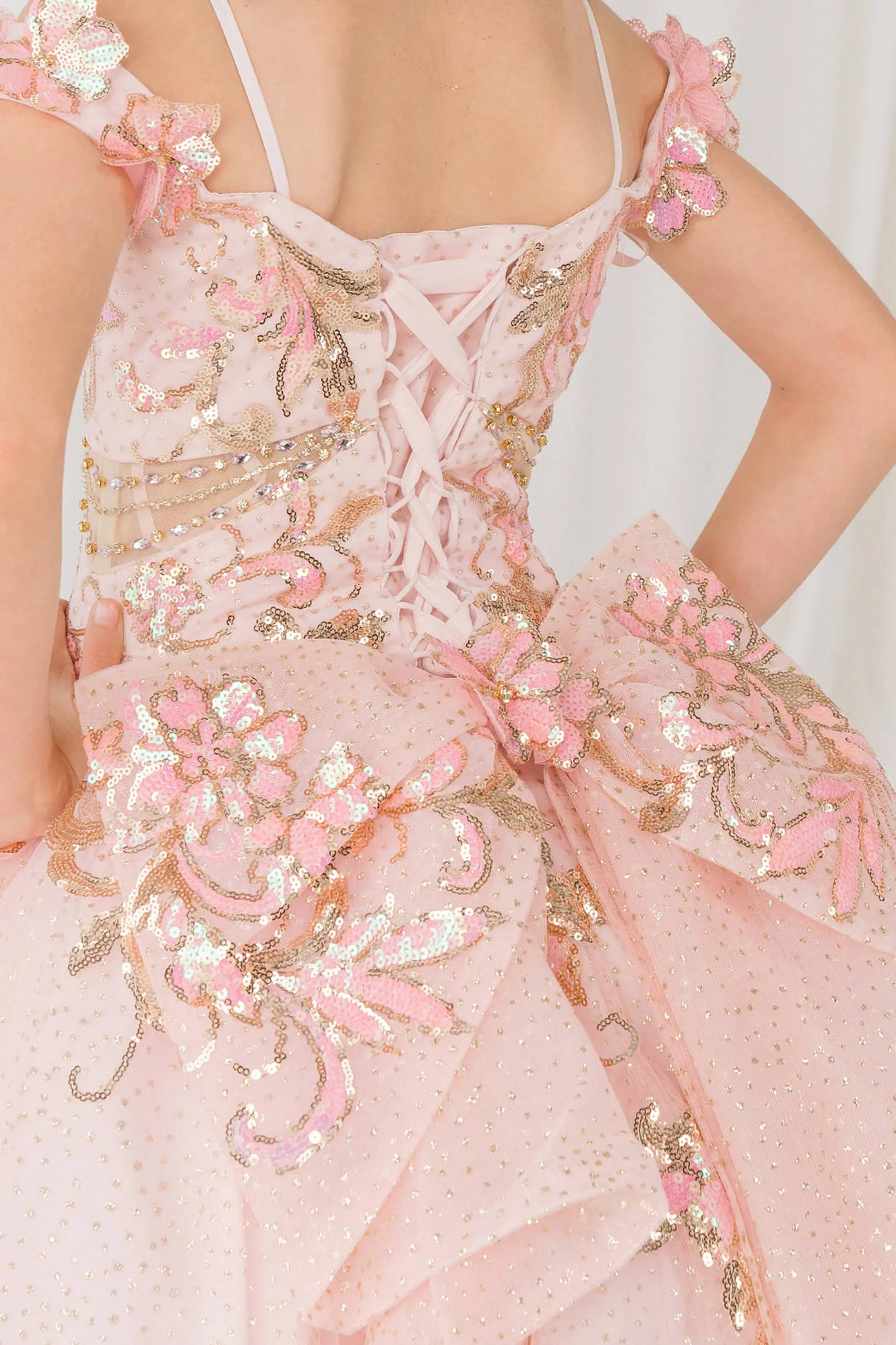 Back close up view of Pink mini quince ball gown with off shoulder floral embroidered bodice, glitter tulle skirt, lace up back, and layered bow