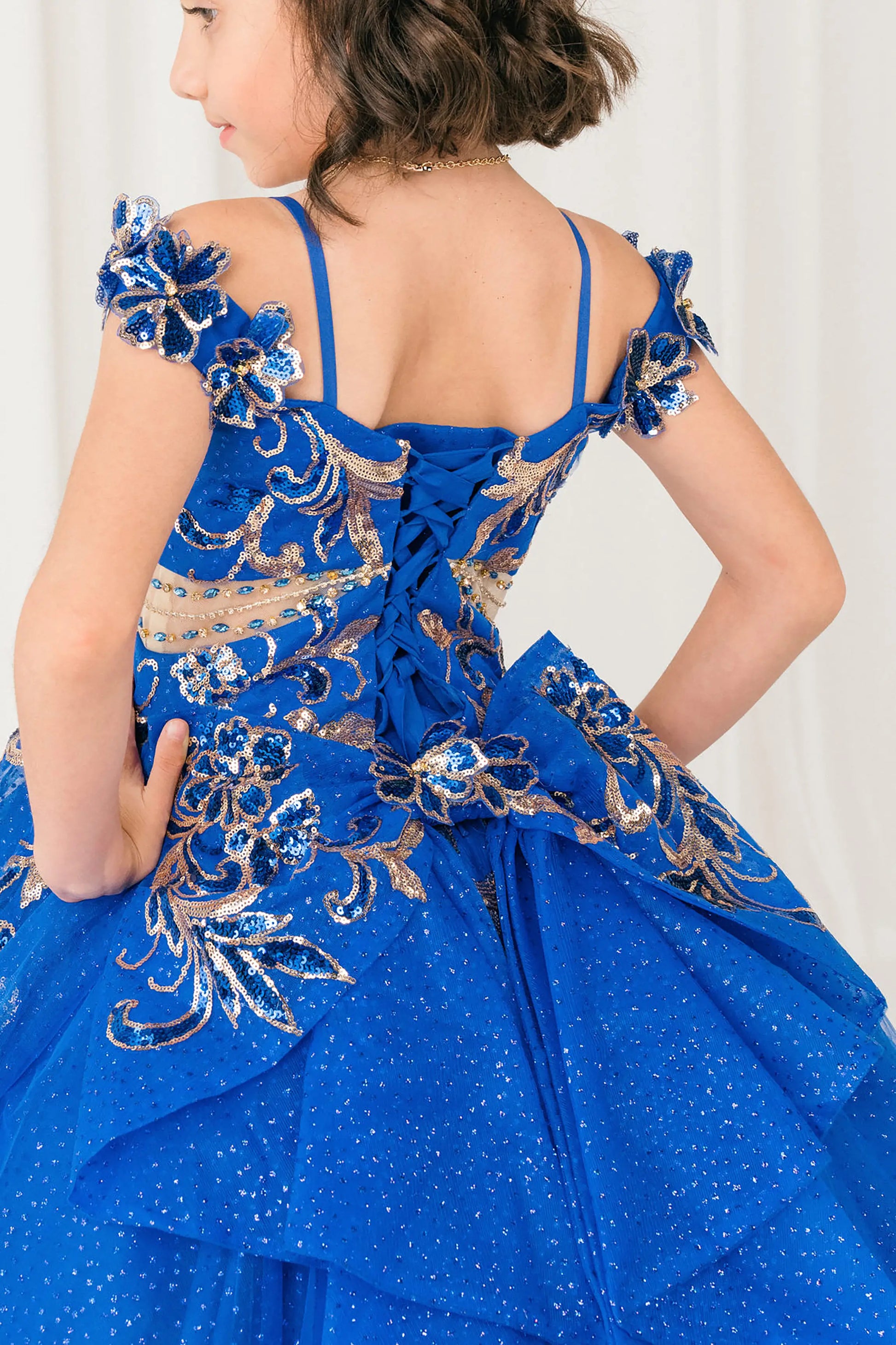 Back close up view of Royal mini quince ball gown with off shoulder floral embroidered bodice, glitter tulle skirt, lace up back, and layered bow