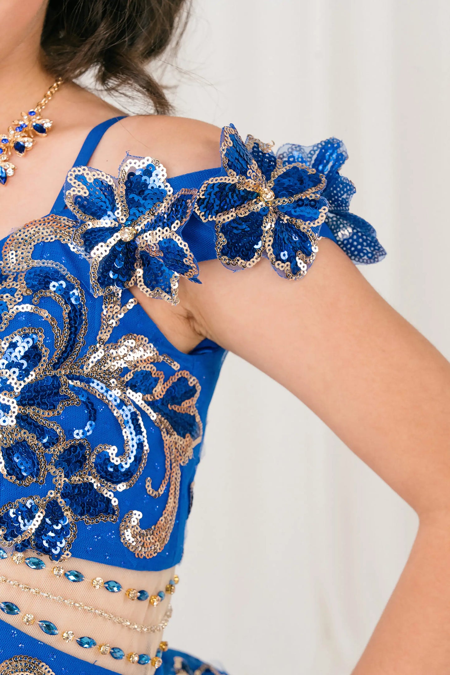 Side close up view of Royal mini quince ball gown with off shoulder floral embroidered bodice, glitter tulle skirt, lace up back, and layered bow