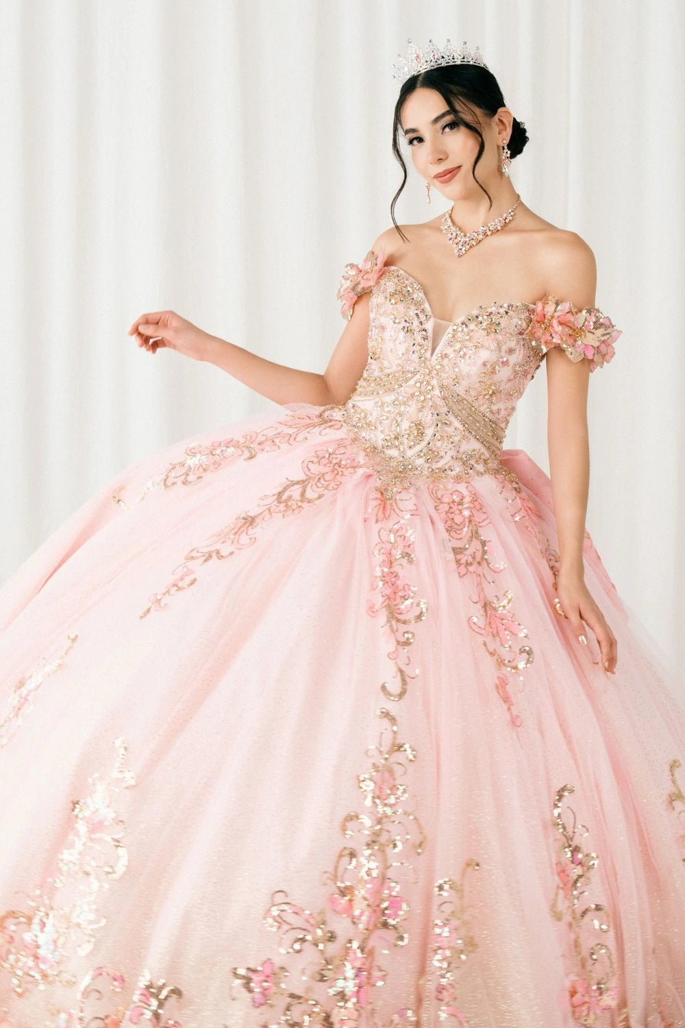 Shown in a upper-front view, the Pink quinceañera dress has off-shoulder floral bodice and gold appliques over the skirt.