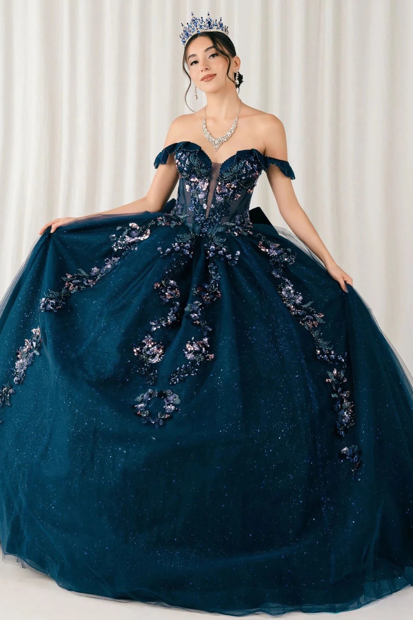 Woman wearing navy quinceañera royal dress with embroidered beaded corset bodice, shimmering textured skirt, cathedral train, detachable cape, and gloves