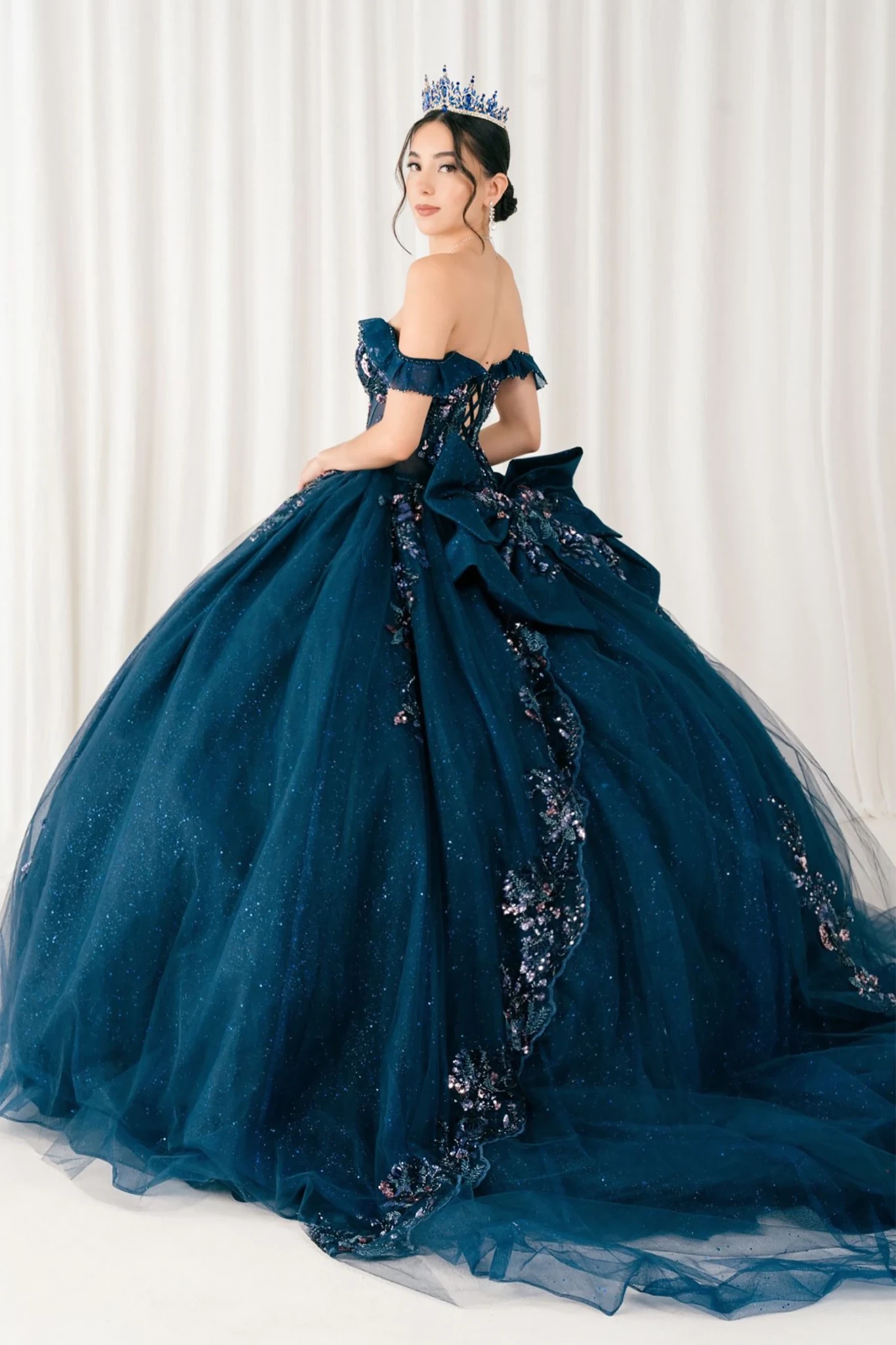 Woman wearing navy quinceañera royal dress side-facing with embroidered beaded corset bodice, shimmering textured skirt, detachable cape, cathedral train, and gloves