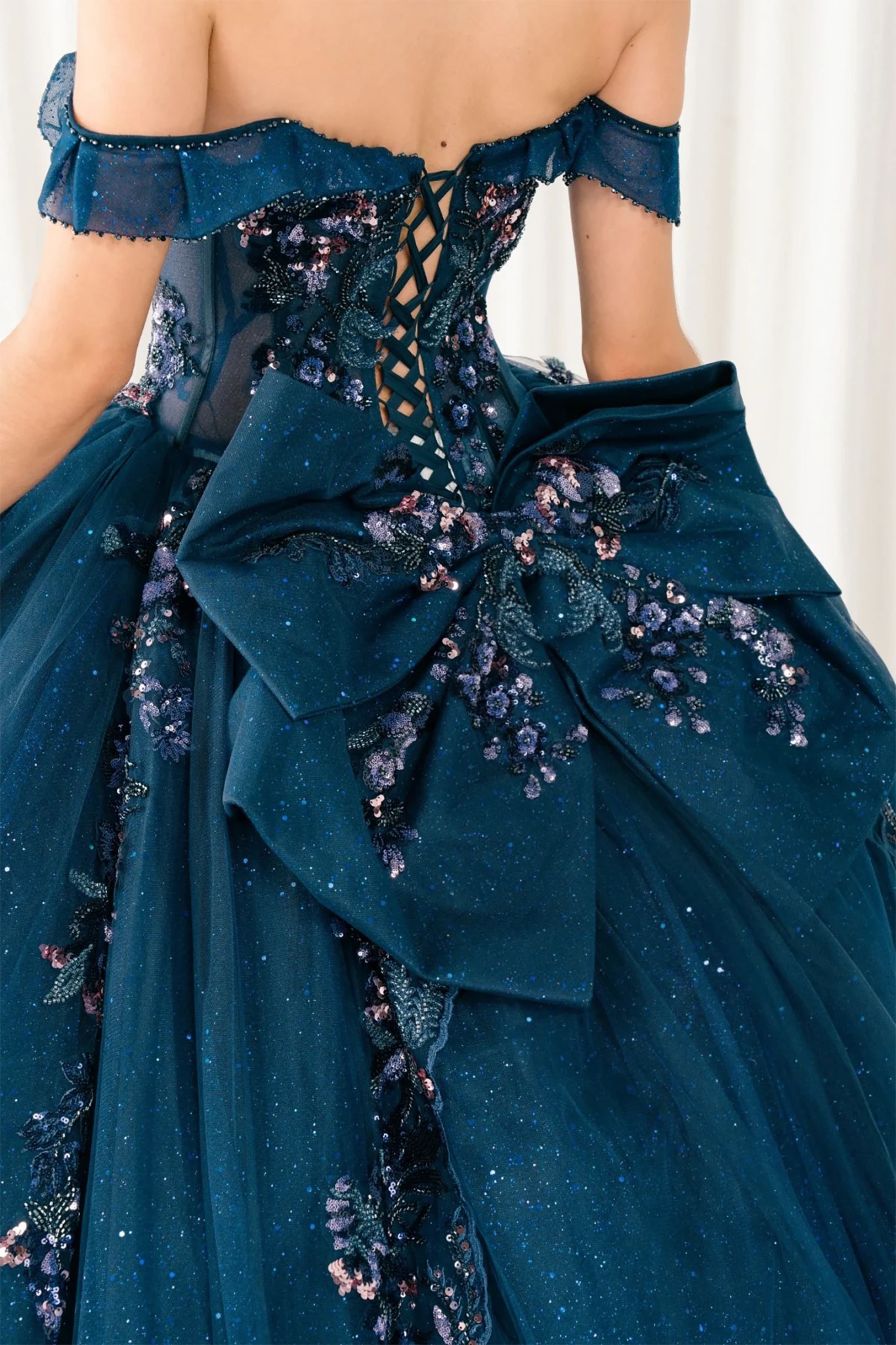 Close-up of woman back-facing in navy quinceañera royal dress with lace-up beaded corset bodice, detachable cape, shimmering textured skirt, cathedral train, and gloves
