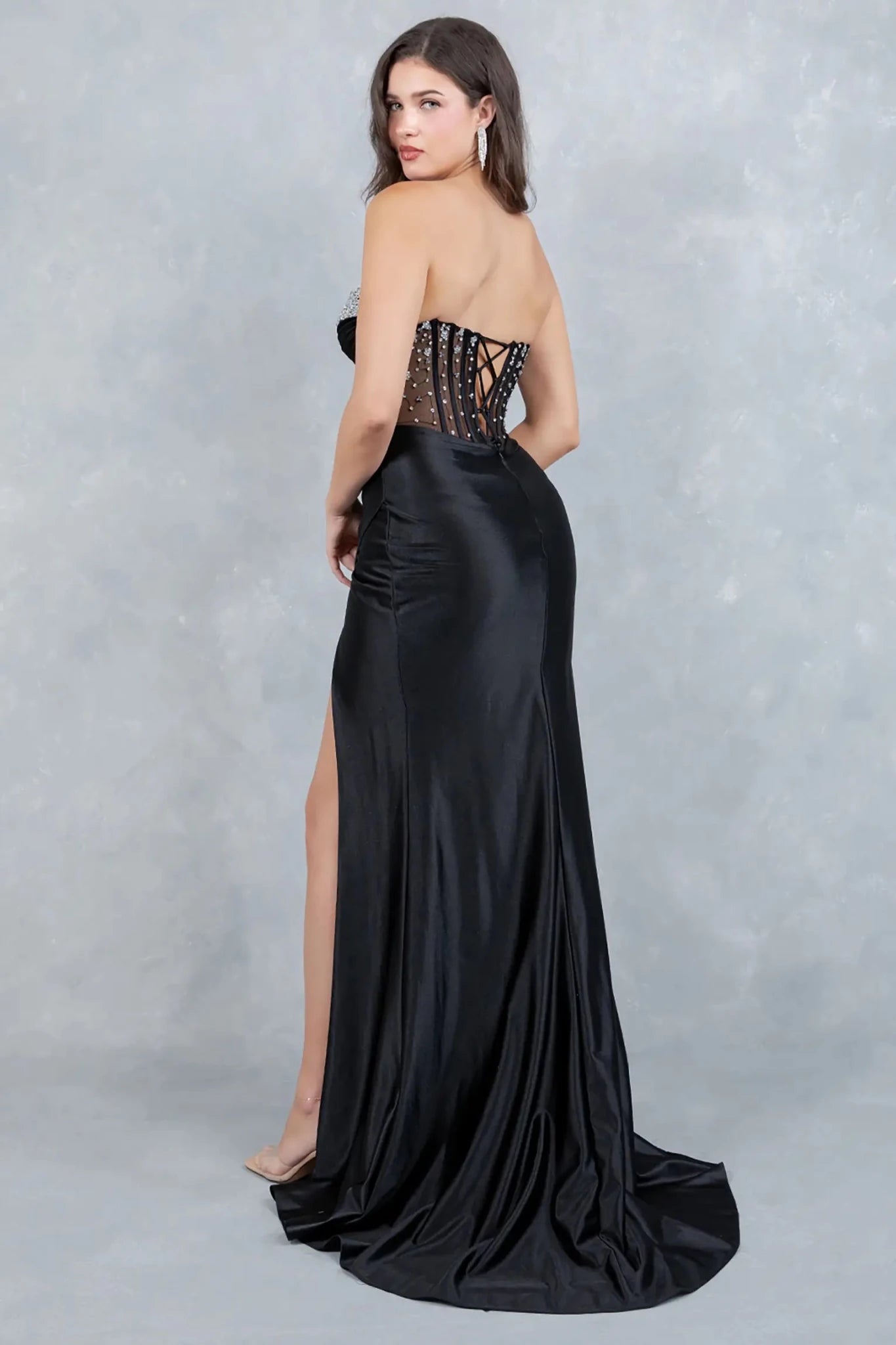 A full-length view of a woman wearing black formal prom dress with a lace-up corset and sweeping train.