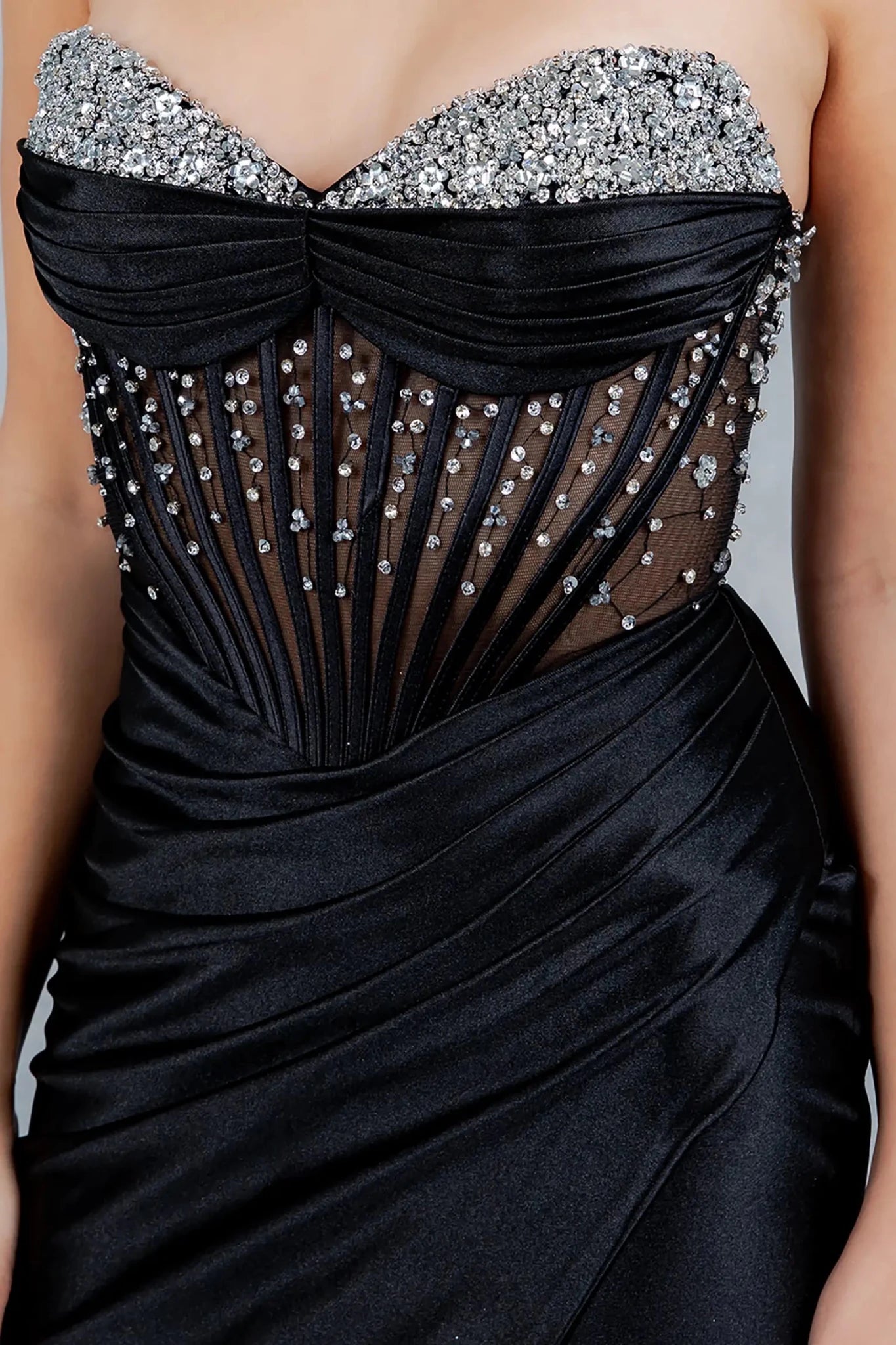 A close-up view highlighting a woman wearing a black strapless bodice adorned with crystals, sequins, and sheer corset boning.