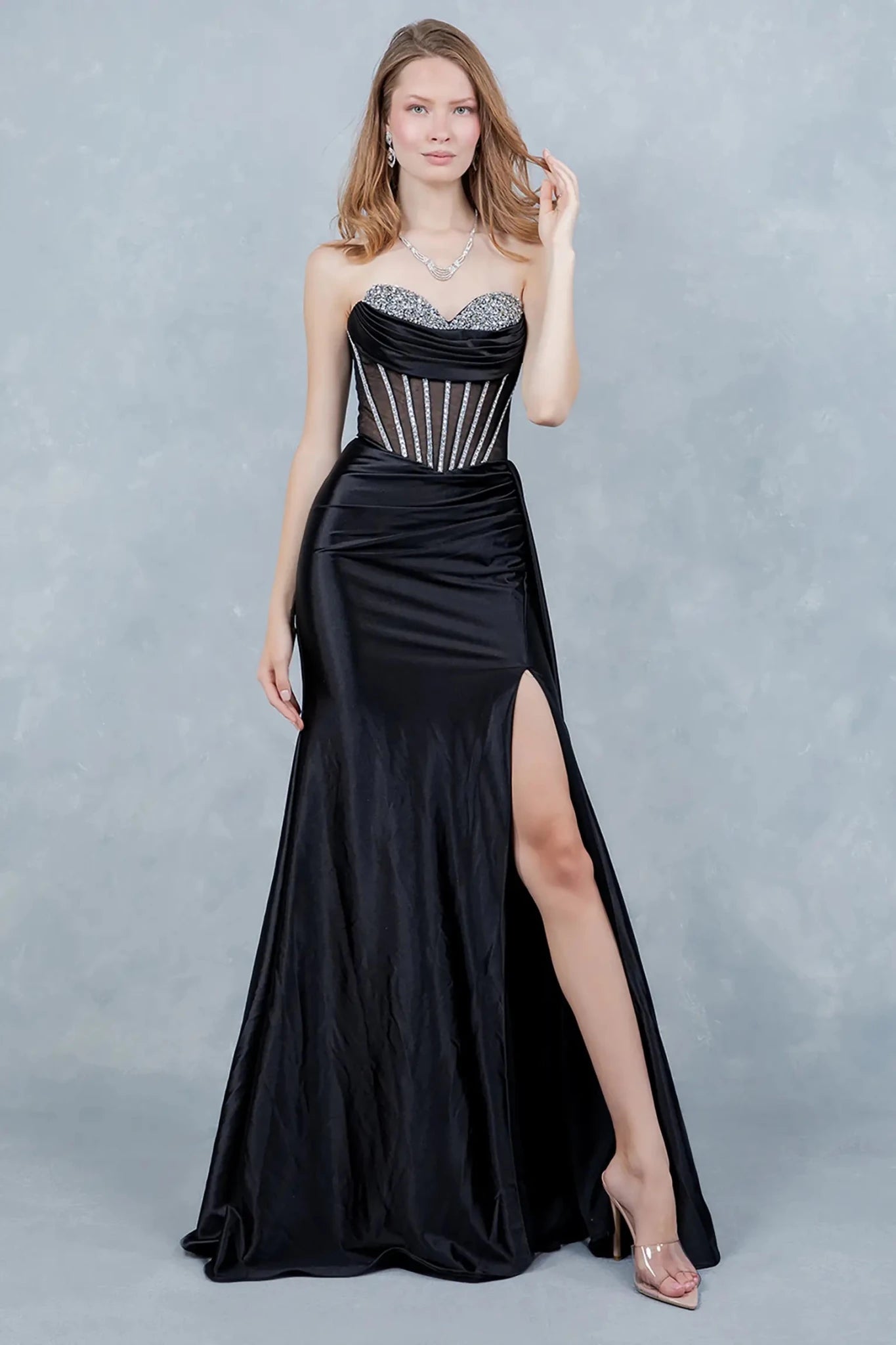 A full-length view of a woman wearing black formal prom dress with a lace-up corset and flowing train.