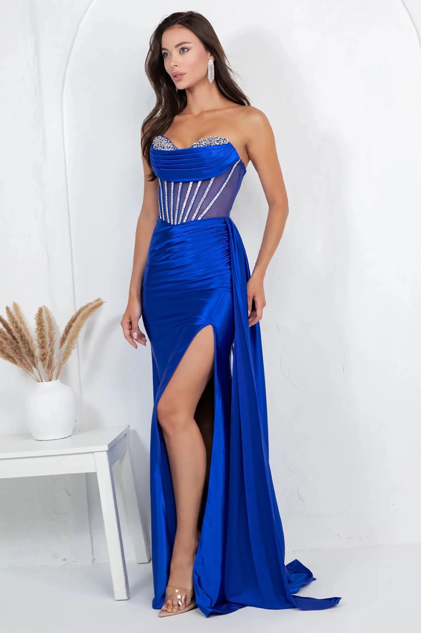 A full-length front view of a woman wearing a blue formal prom dress designed with a lace-up corset and trailing train.