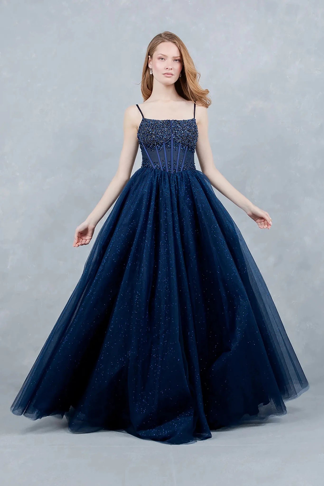 A full-length view of a woman wearing navy fairytale prom dress with a lace-up corset and glitter tulle skirt.
