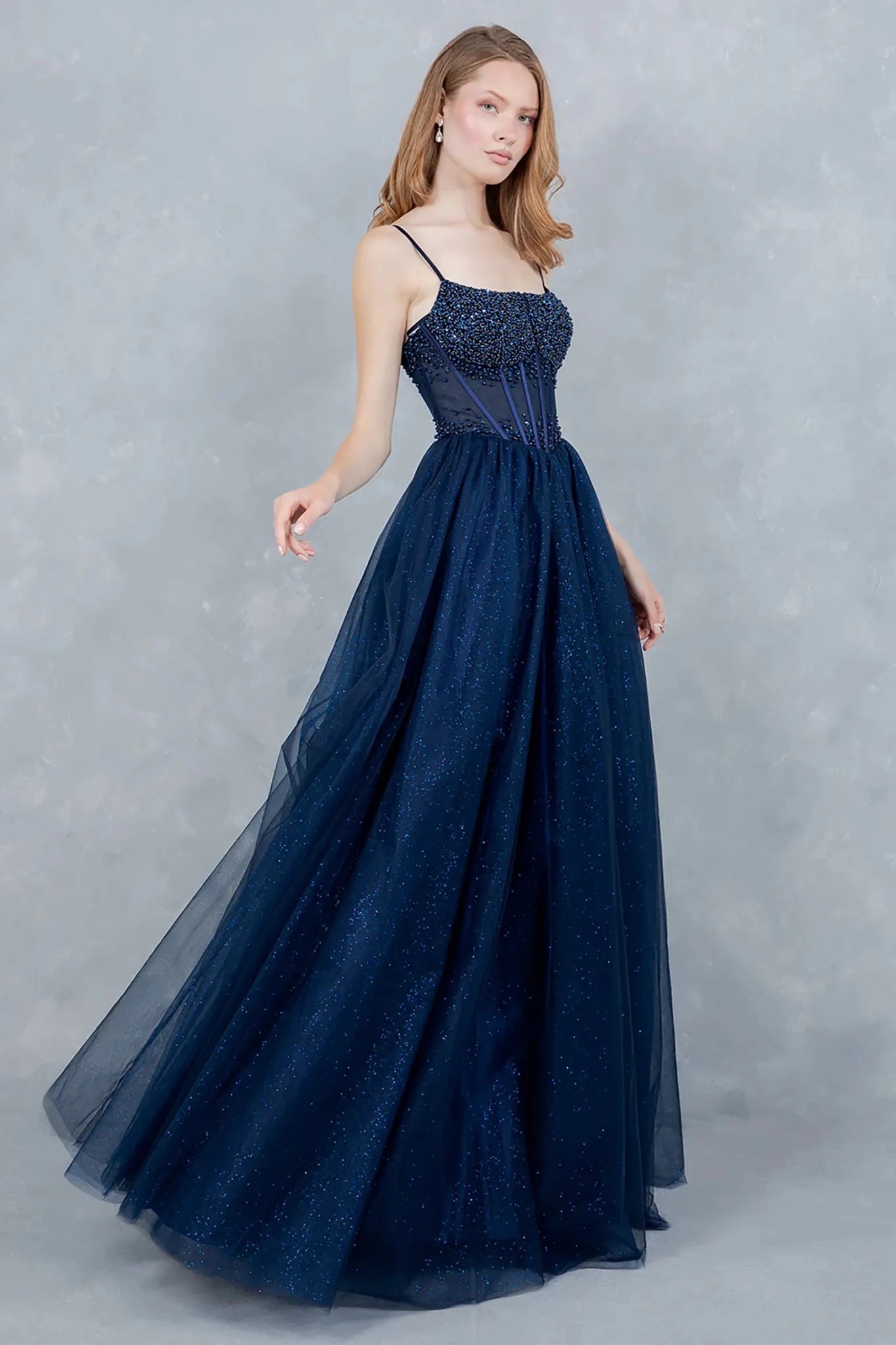 A side profile view of a woman wearing a navy prom dress, highlighting the dramatic volume and flowing tulle silhouette.