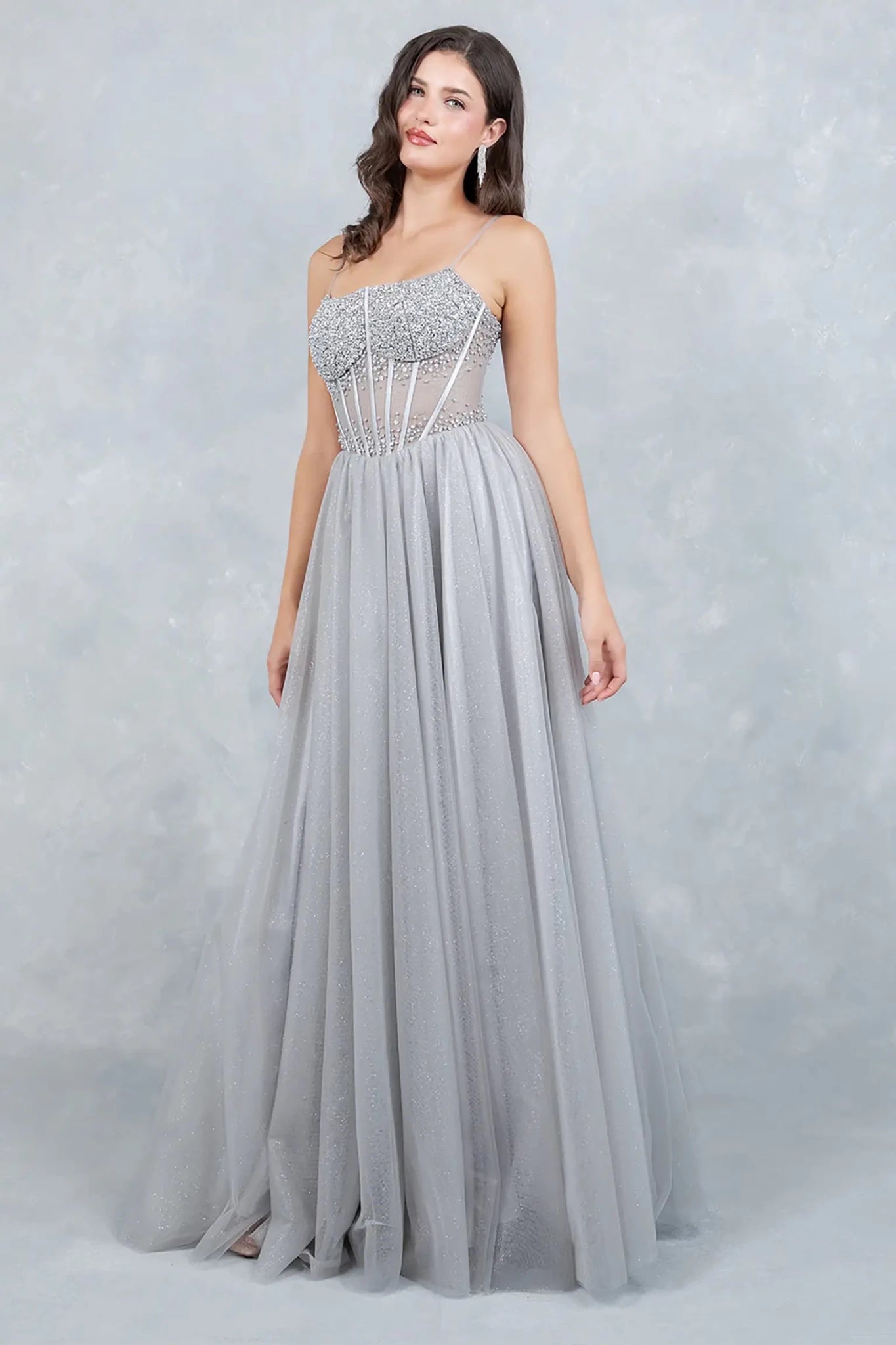 A side profile view of a woman wearing a silver prom dress, showcasing the sculpted waist and dramatic tulle volume.