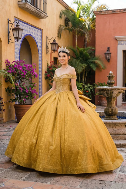 Woman wearing gold off-shoulder ball gown side-facing with beaded corset bodice, shimmering glitter tulle layers, and flowing silhouette