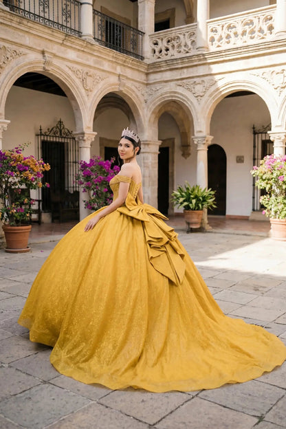Woman wearing gold off-shoulder ball gown side-facing with beaded corset bodice, shimmering glitter tulle layers, and flowing silhouette