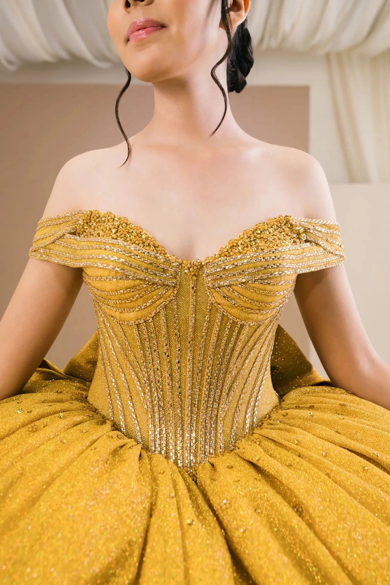 Close-up of woman wearing gold off-shoulder sweetheart ball gown with beaded corset bodice, glitter detailing, and elegant neckline
