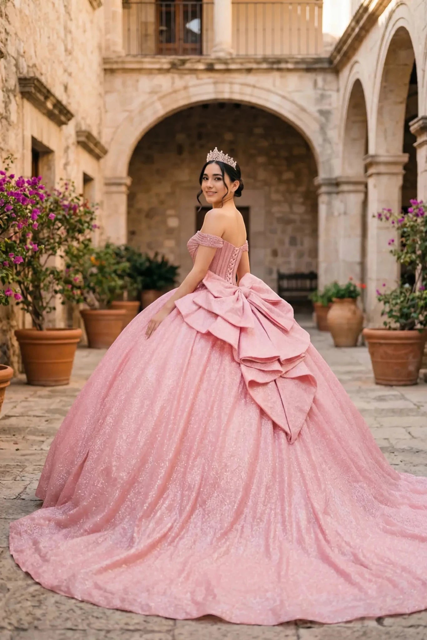 Woman wearing rose gold off-shoulder ball gown side-facing with beaded corset bodice, shimmering glitter tulle layers, and flowing silhouette