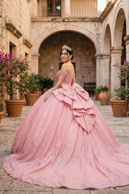 Woman wearing rose gold off-shoulder ball gown side-facing with beaded corset bodice, shimmering glitter tulle layers, and flowing silhouette