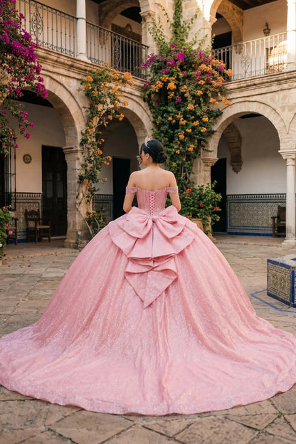 Woman back-facing in rose gold off-shoulder ball gown with lace-up corset bodice, intricate beadwork, glitter tulle, and cascading full skirt