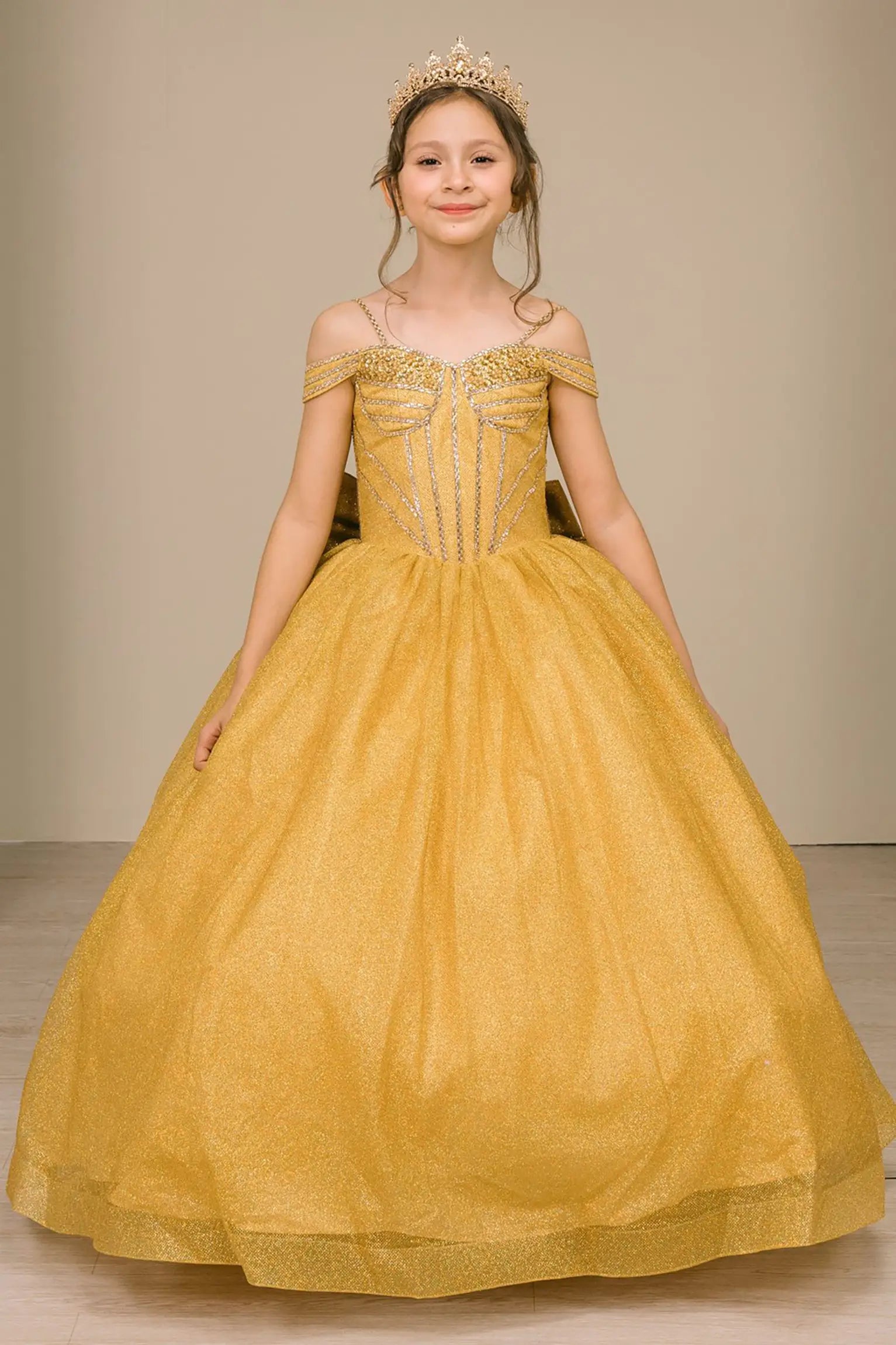 Kid standing front-facing in enchanting gold ball gown with oversized tiered bow accent, fitted bodice, and voluminous layered skirt

