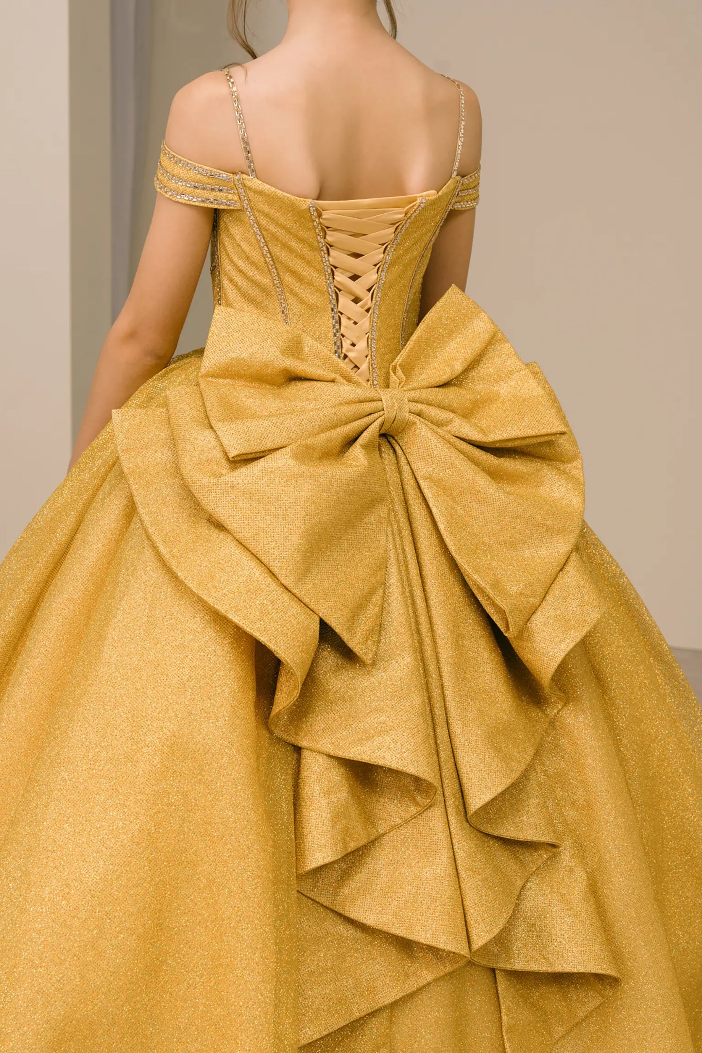 Kid standing three-quarter view in gold ball gown with oversized tiered bow, glittering bodice, and dramatic layered skirt

