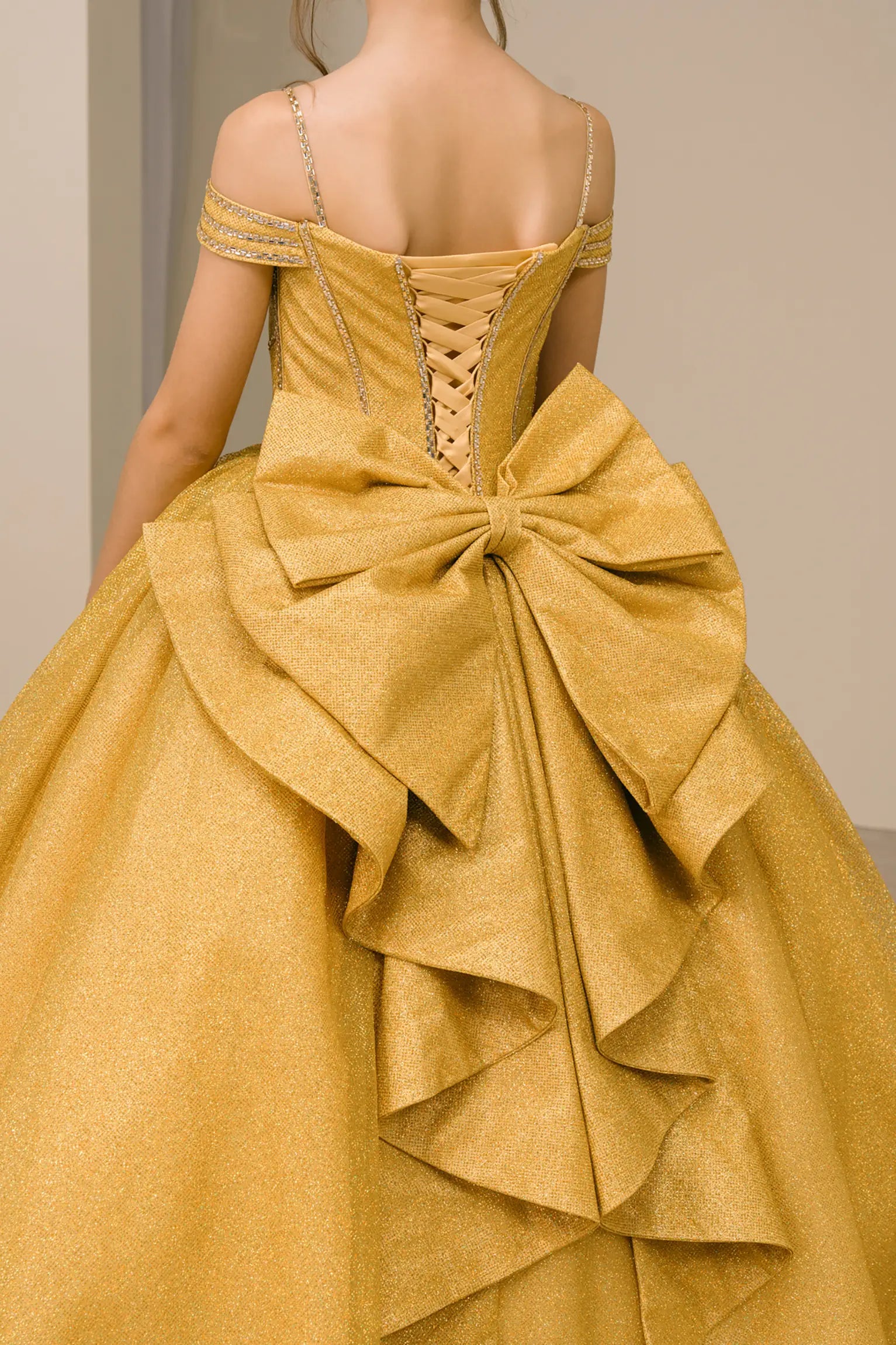 Kid standing three-quarter view in gold ball gown with oversized tiered bow, glittering bodice, and dramatic layered skirt

