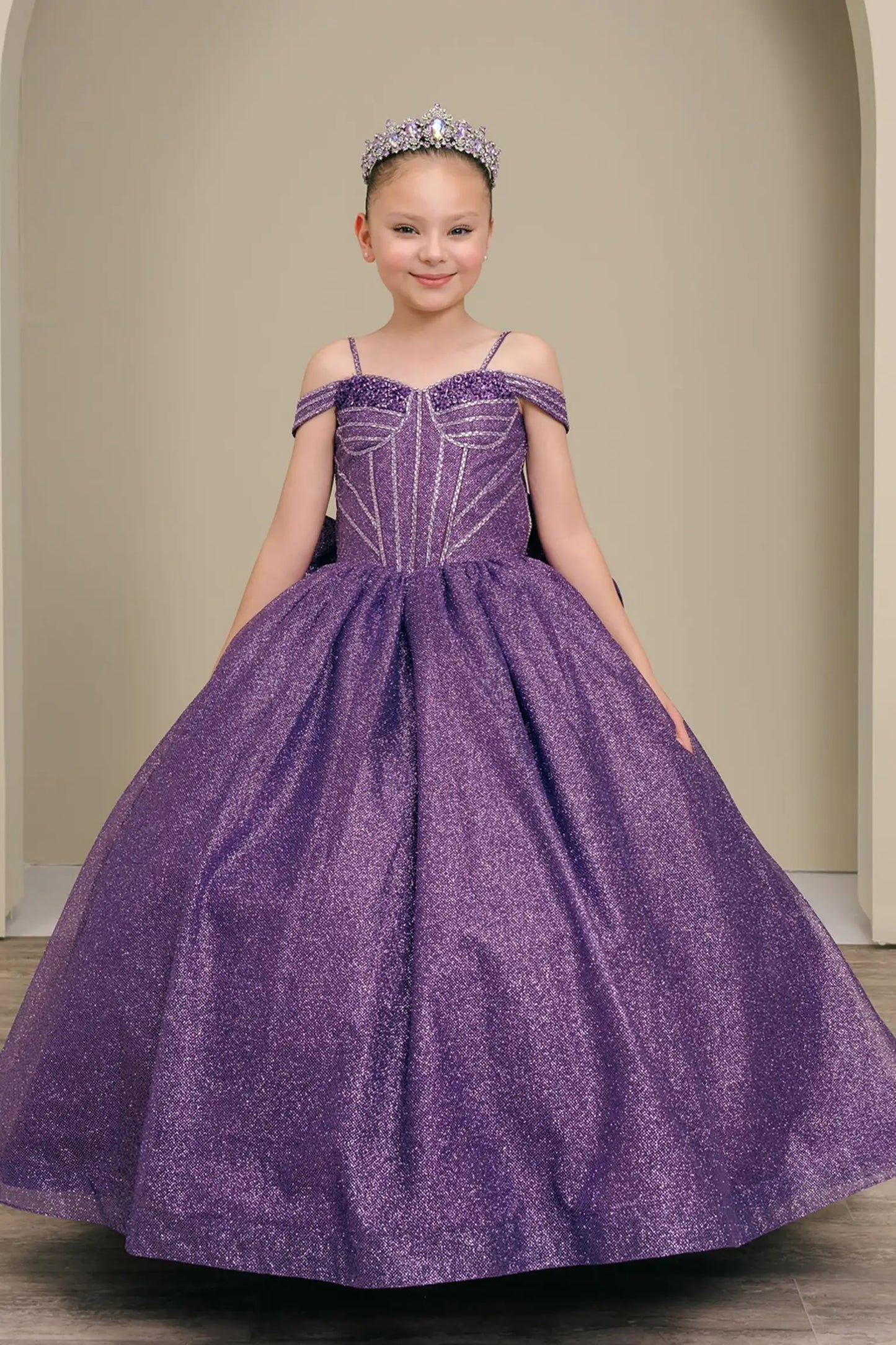 Kid standing front-facing in enchanting purple ball gown with oversized tiered bow accent, fitted bodice, and voluminous layered skirt

