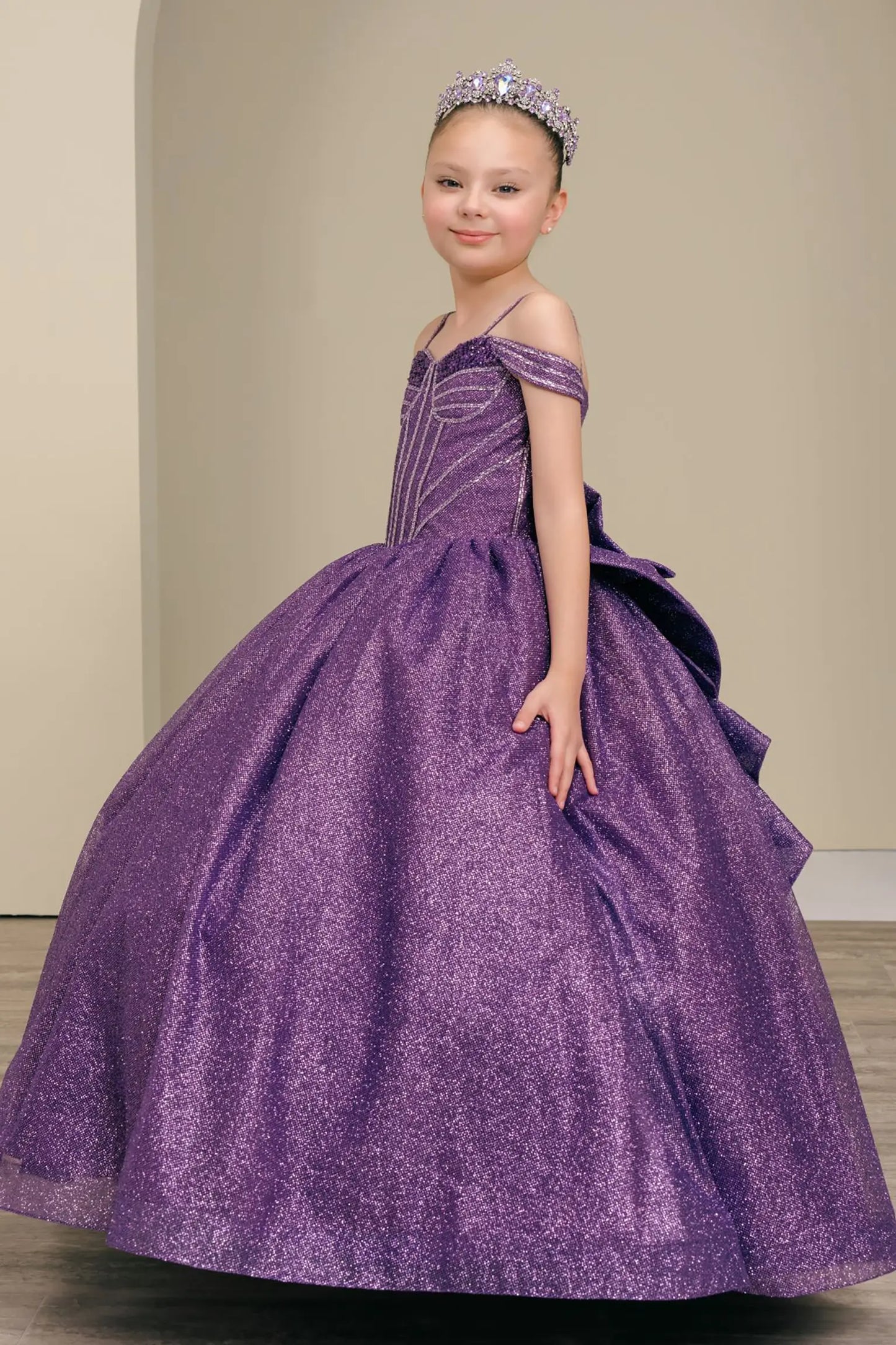 Kid standing side-facing in purple ball gown with oversized tiered bow detail, shimmering bodice, and flowing layered skirt

