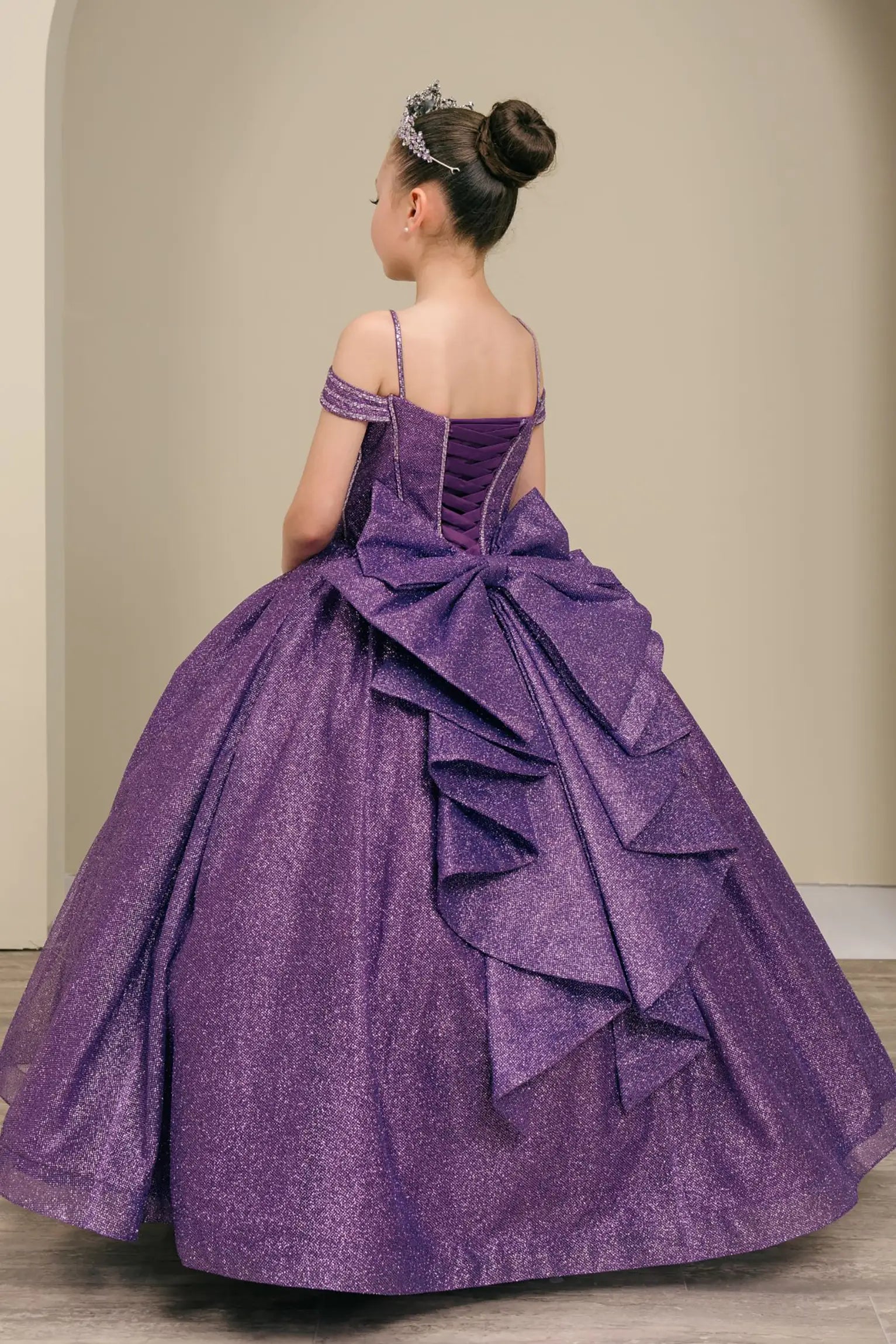 Kid standing three-quarter view in purple ball gown with oversized tiered bow, glittering bodice, and dramatic layered skirt

