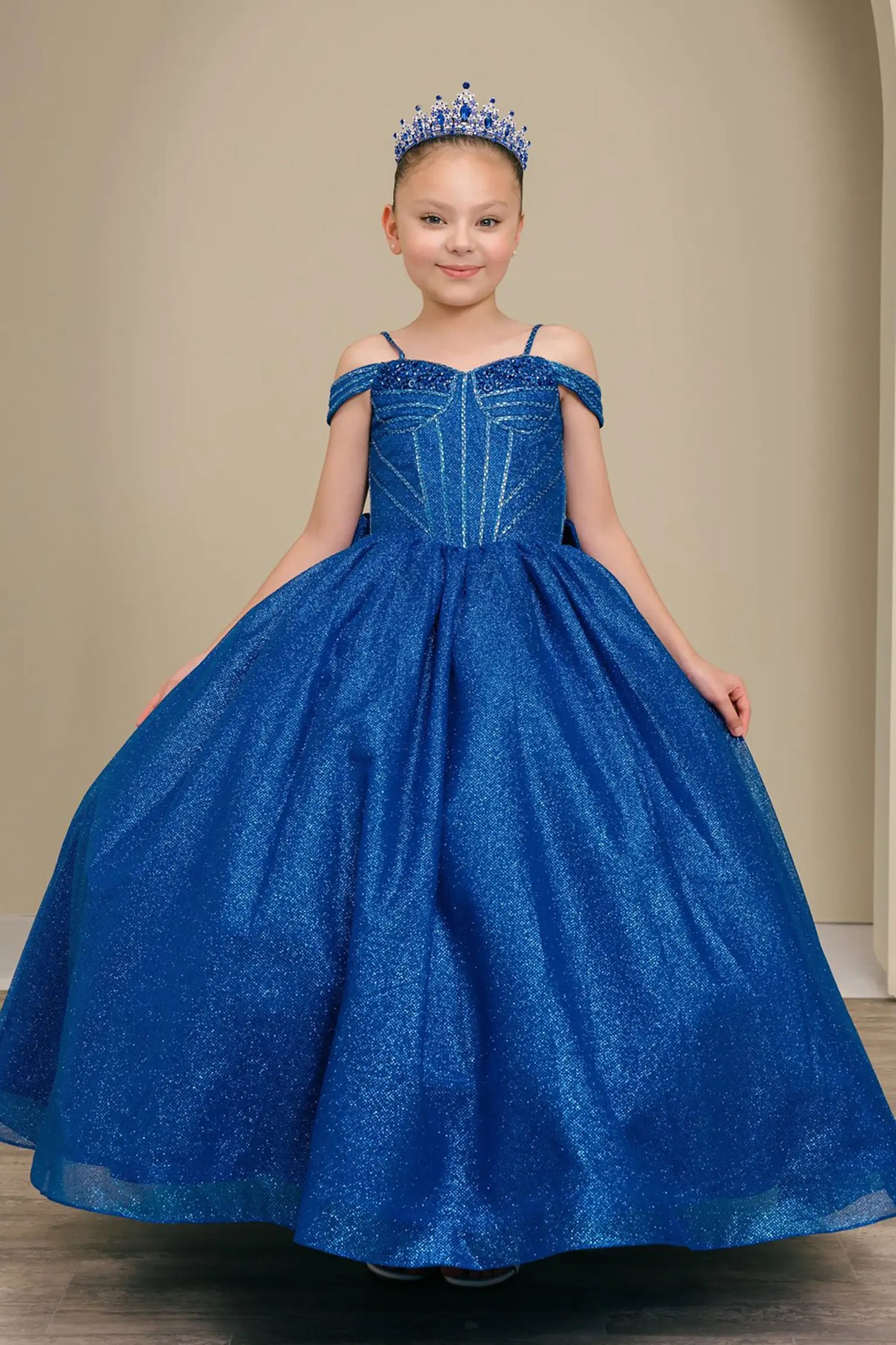 Kid standing front-facing in enchanting royal blue ball gown with oversized tiered bow accent, fitted bodice, and voluminous layered skirt

