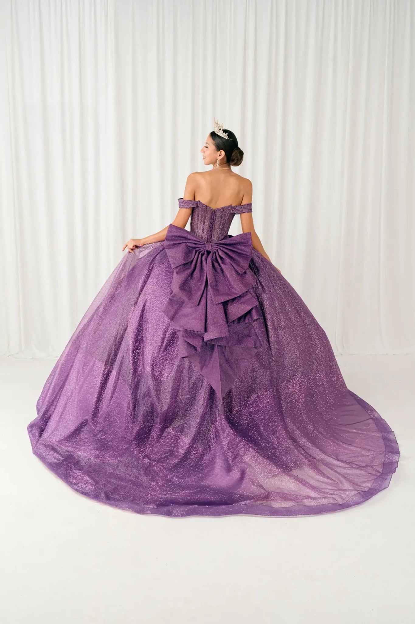 Woman standing back-facing in purple ball gown with lace-up corset bodice and cascading glitter tulle skirt


