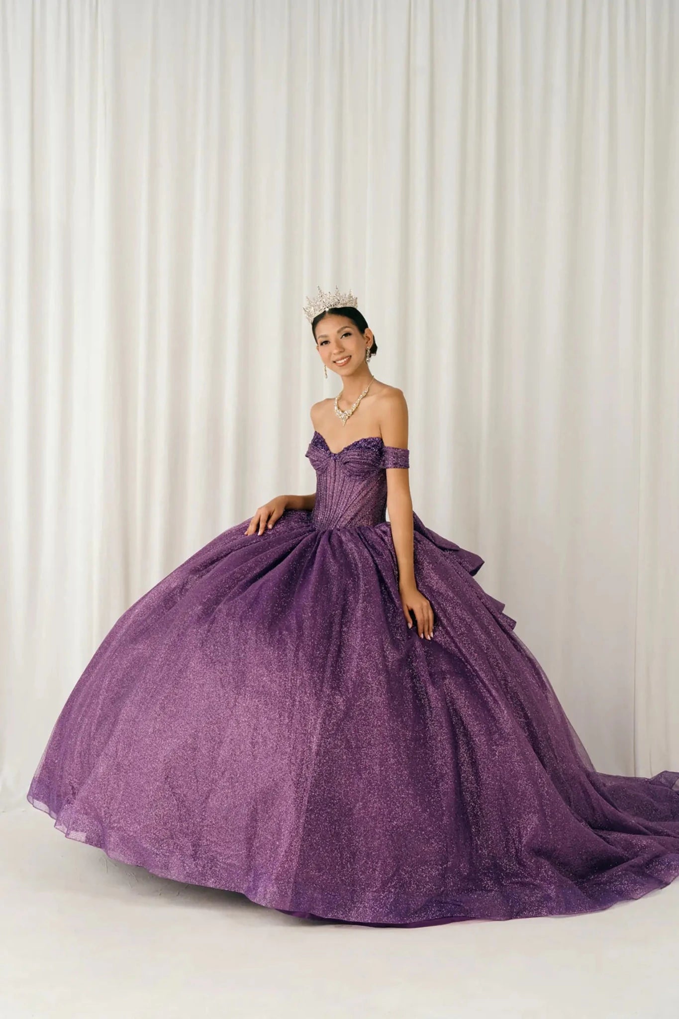 Woman standing three-quarter view in purple ball gown with shimmering beaded corset bodice and dramatic glitter tulle skirt

