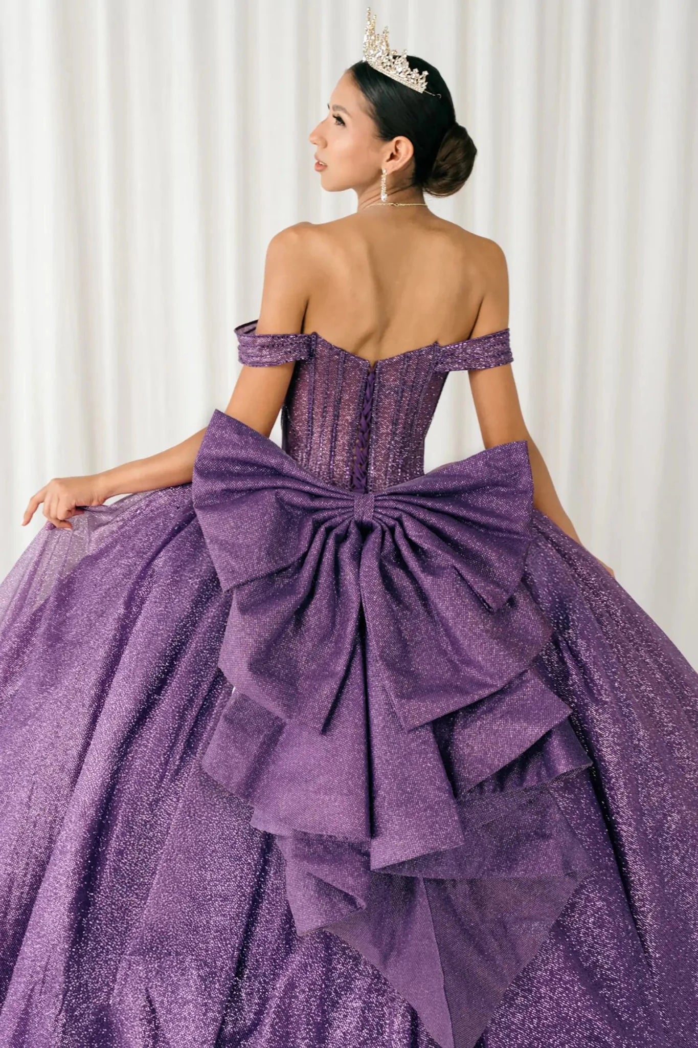 Woman standing back-facing in purple ball gown with lace-up corset bodice and cascading glitter tulle skirt

