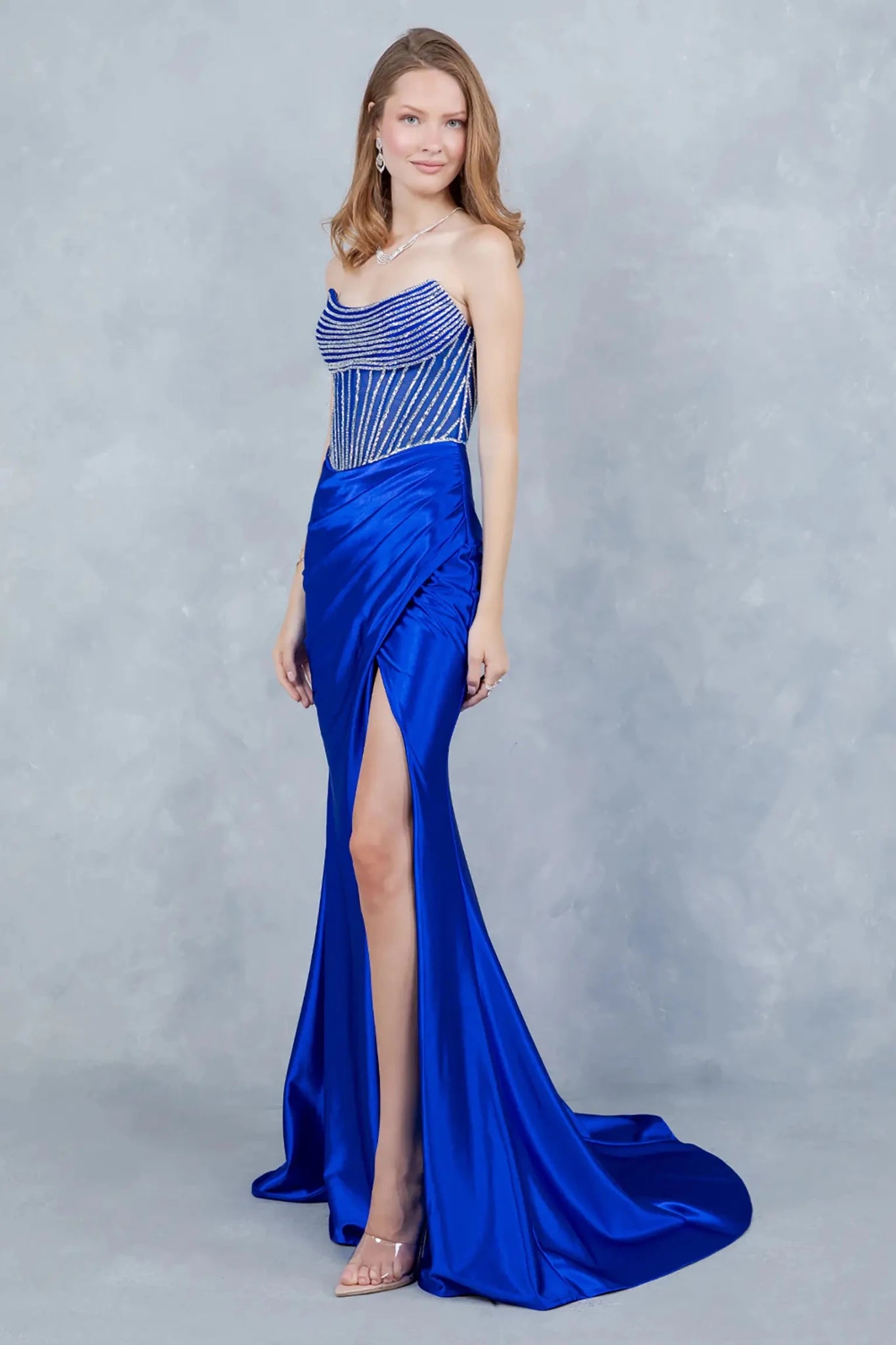 A side profile view of a woman wearing a blue satin prom dress, highlighting its sculpted silhouette and thigh-high slit.