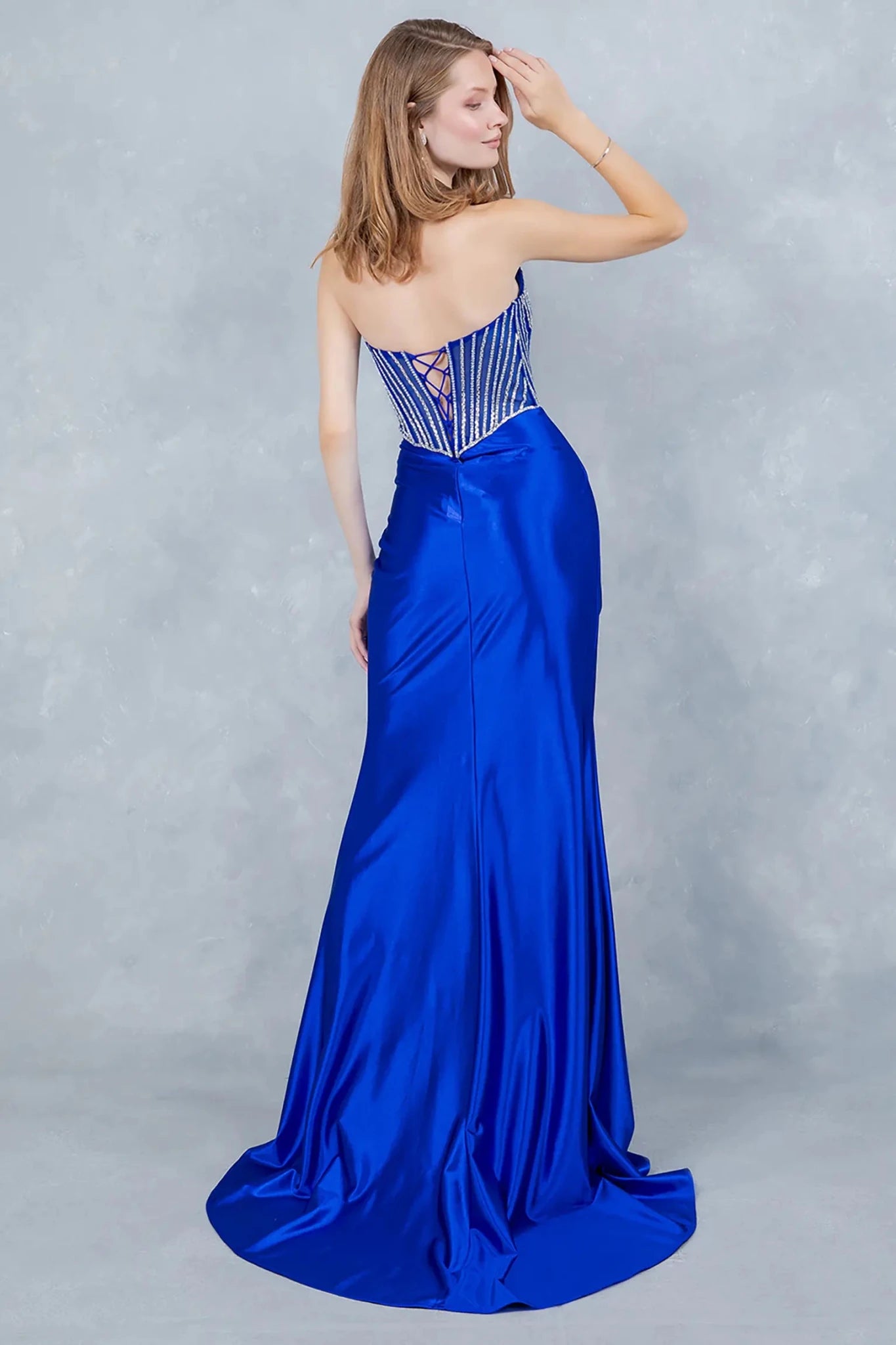 A full back view of a woman wearing a blue formal dress with a lace-up corset and flowing train.