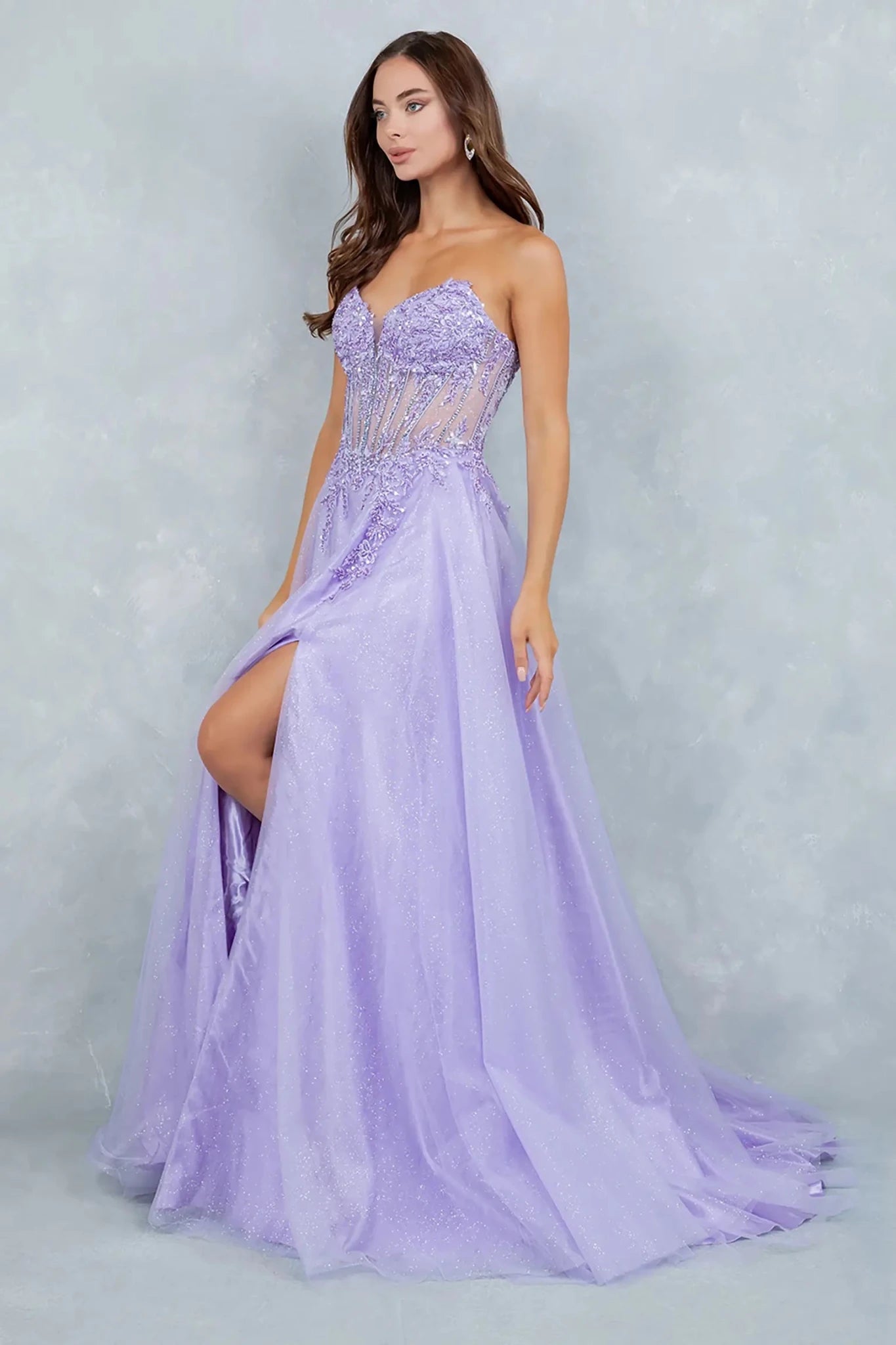 A side profile view of a woman wearing a lilac A-line prom dress, highlighting the sculpted corset waist and flowing glitter tulle skirt.