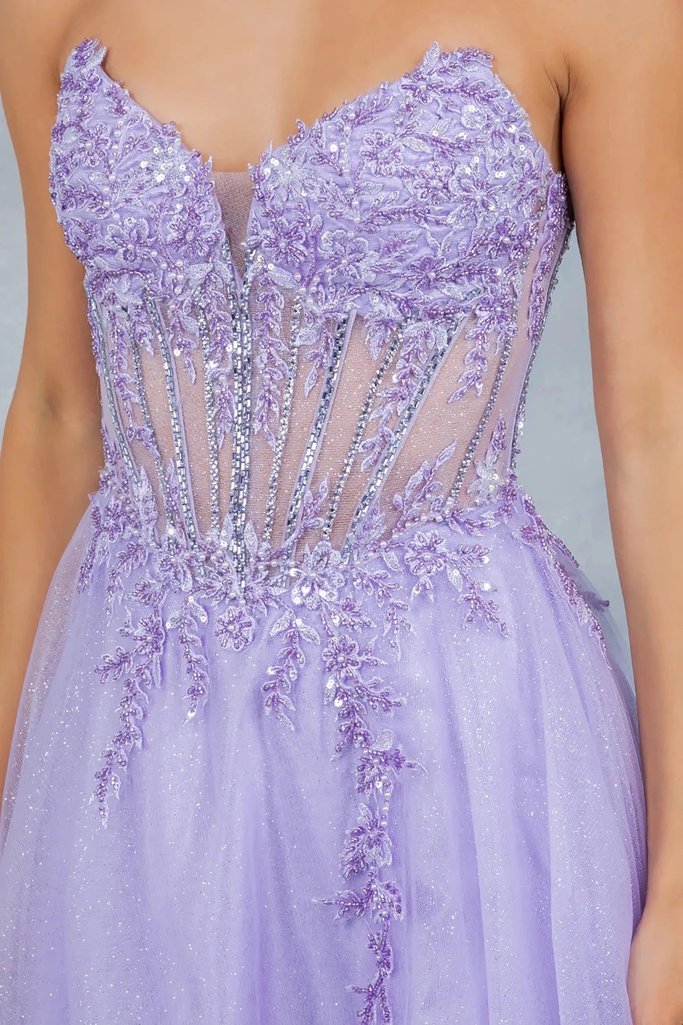 A close-up view of a woman wearing a lilac strapless bodice with floral lace appliqués, sequins, and sheer corset paneling.
