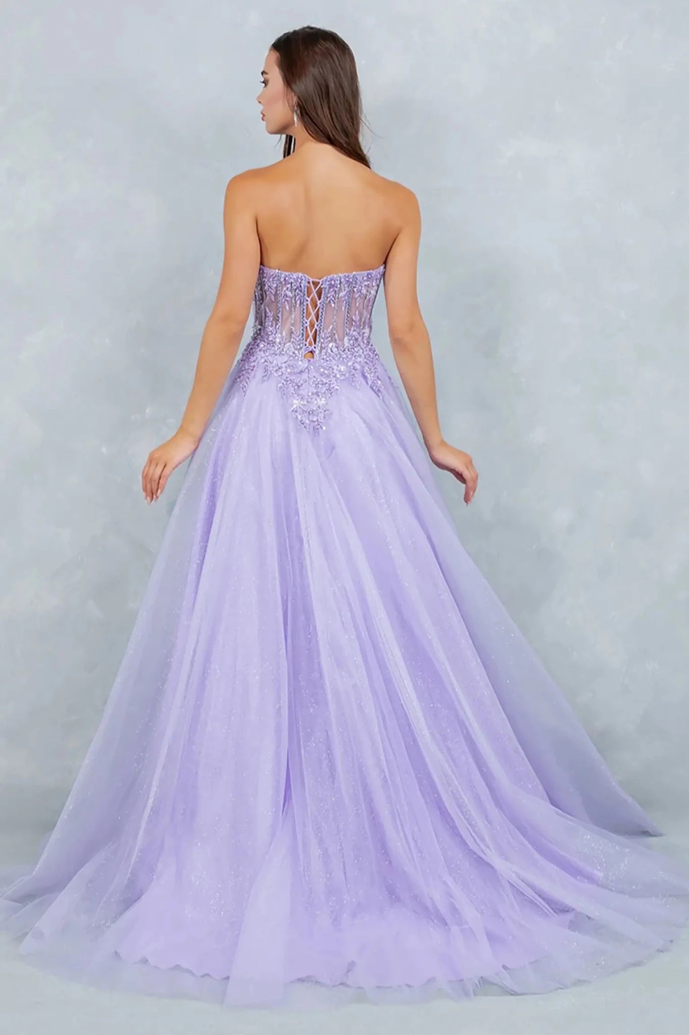 Full back view of a woman wearing a lilac fairytale prom dress designed with a lace-up corset back and layered glitter tulle skirt.