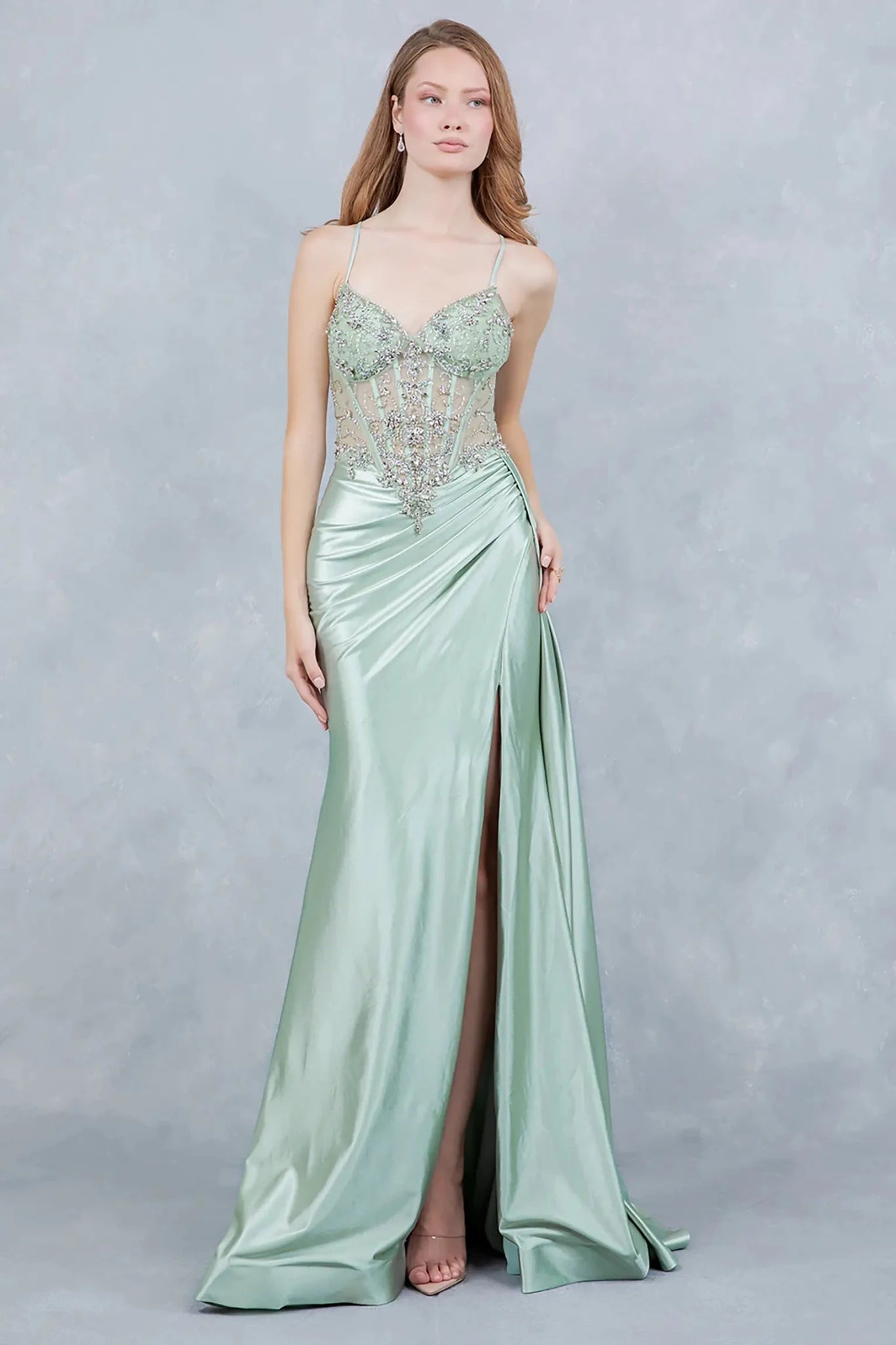 A full-length view of a woman wearing sage formal dress with a lace-up corset and train.
