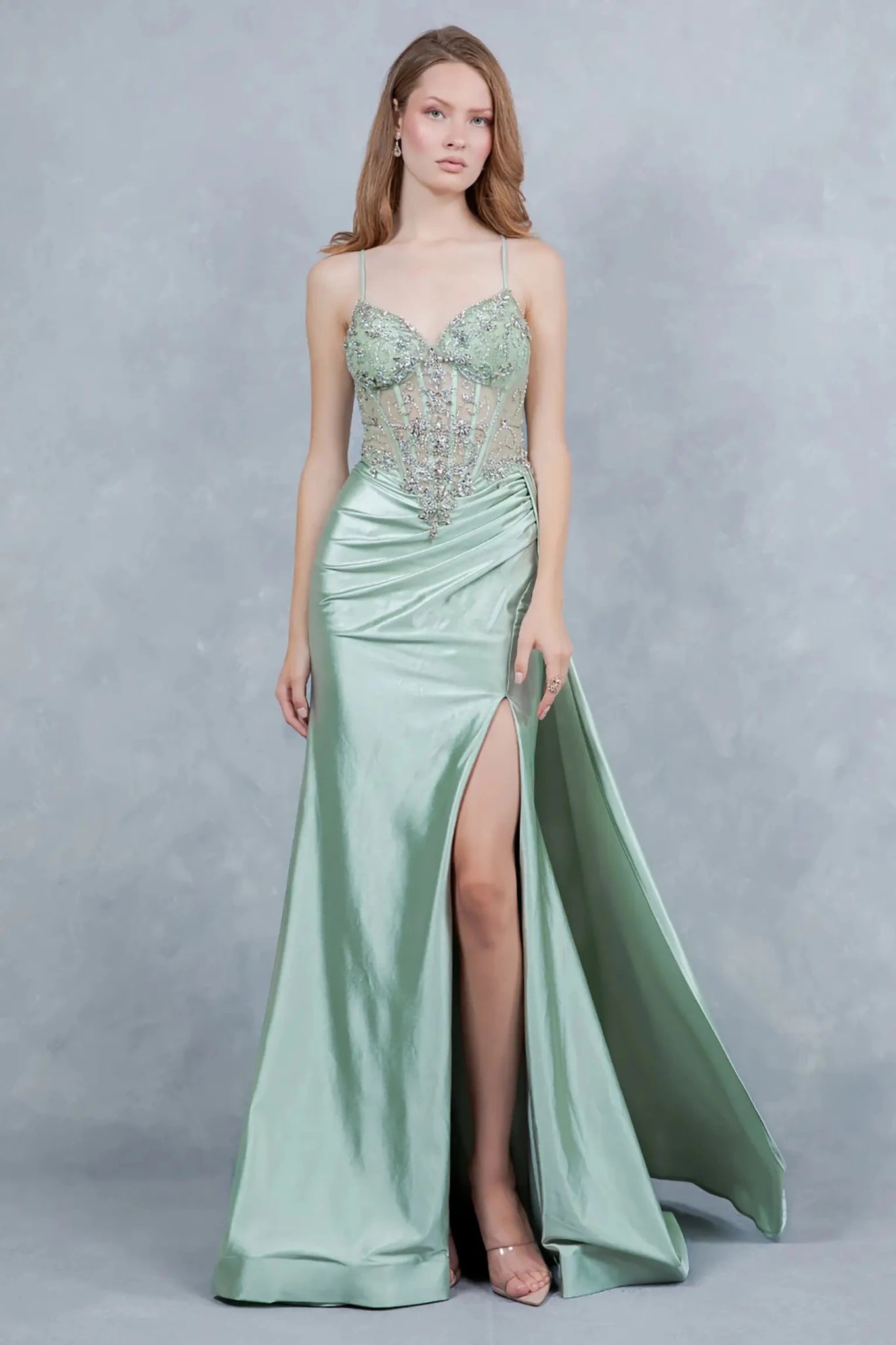 A full-length front view of a woman wearing a sage formal dress with a lace-up corset and train.
