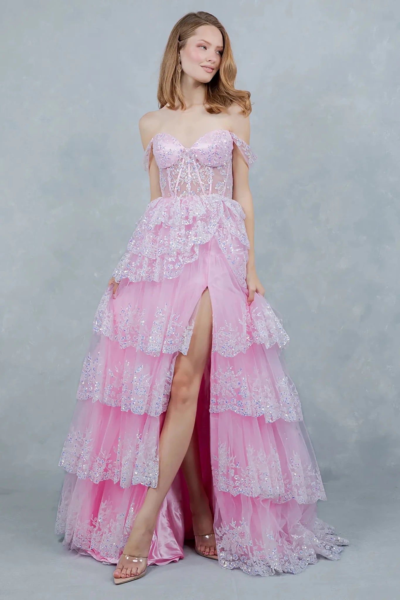 A full-length front view of a woman wearing a pink fairytale dress designed with a lace-up corset and voluminous layered skirt.