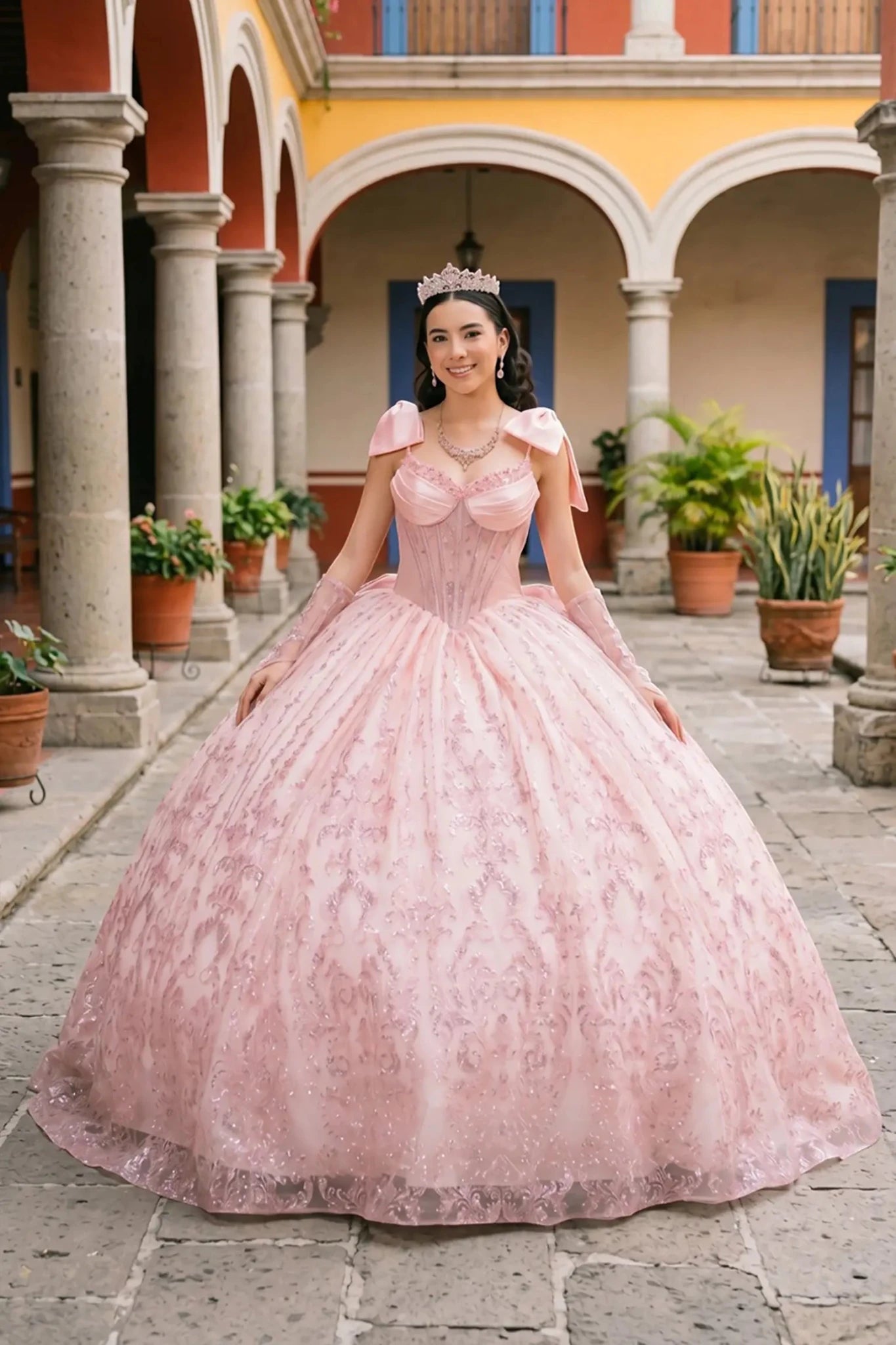 Front view of a woman wearing blush off-shoulder sweetheart quinceañera dress with beaded corset bodice, lace appliqué, and layered tulle skirt