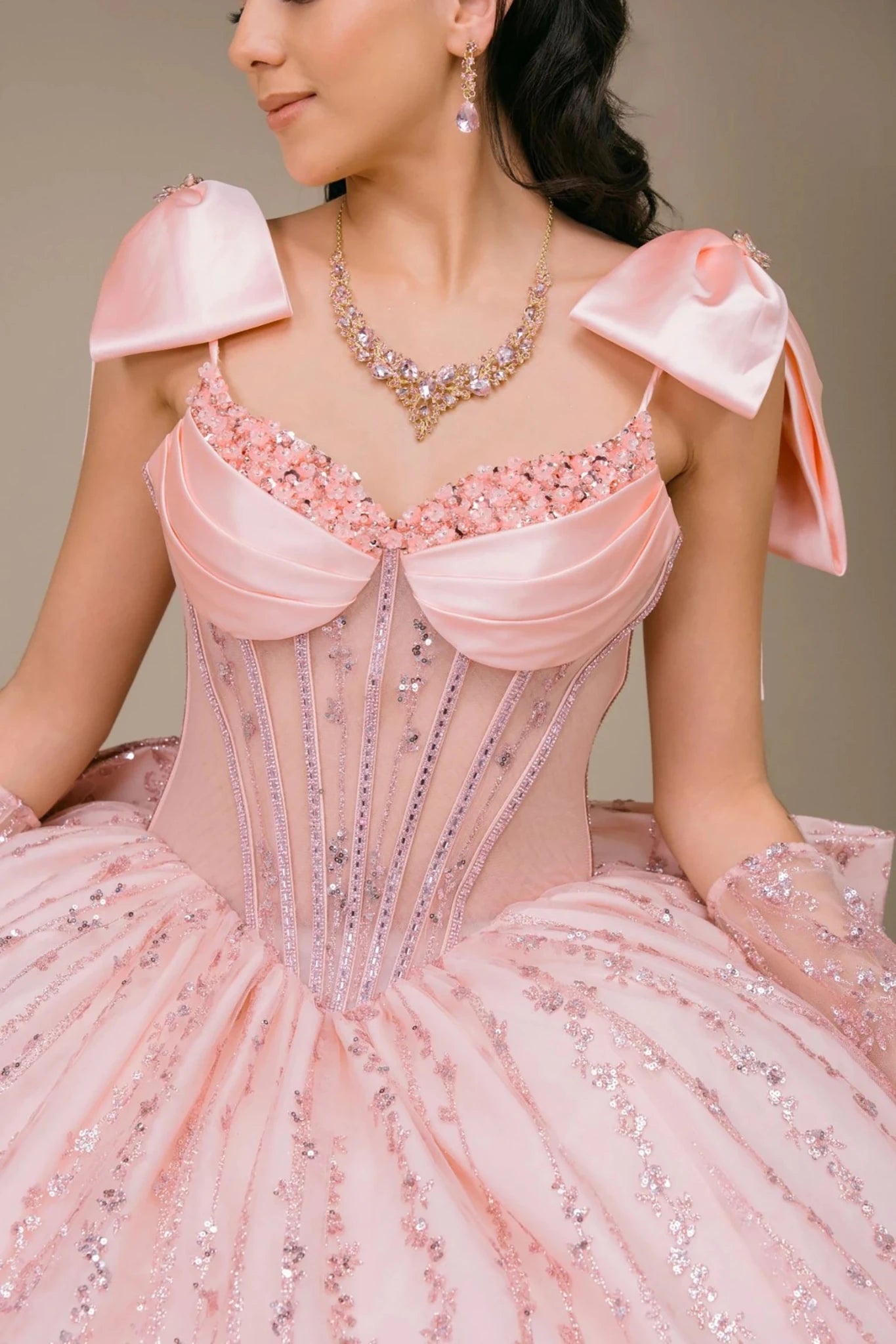 Close-up of woman wearing blush off-shoulder sweetheart quinceañera dress with beaded corset bodice, lace appliqué, and sweetheart neckline