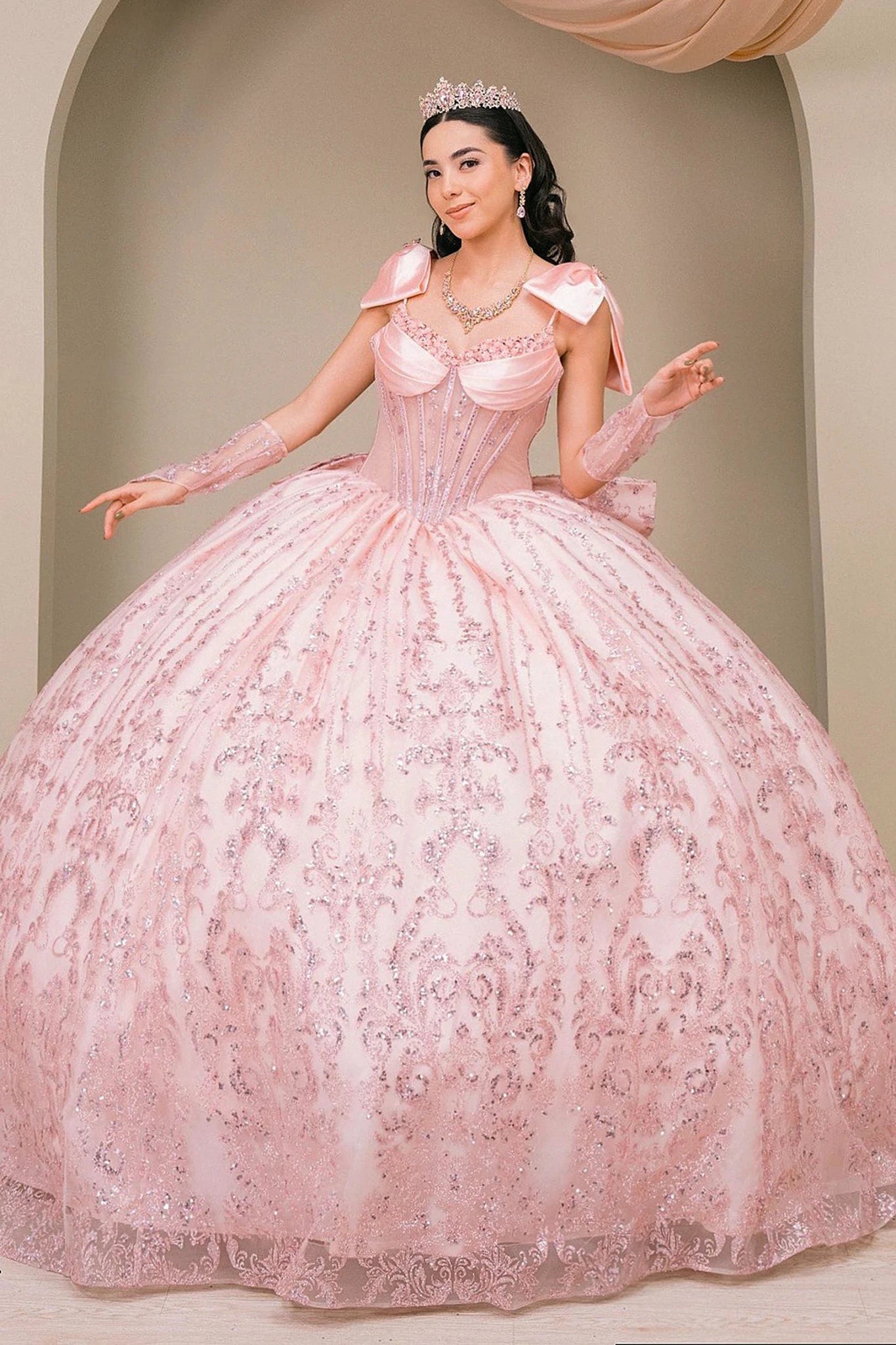 Woman wearing blush off-shoulder sweetheart quinceañera dress with beaded corset bodice, lace appliqué, and layered tulle skirt