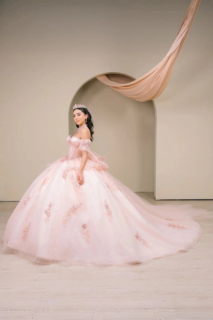 Woman wearing blush off-shoulder sweetheart quinceañera dress side-facing with beaded corset bodice, floral appliqué, oversized bow accent, and cascading train