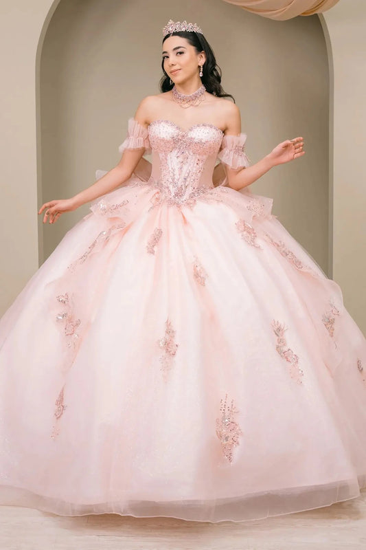 Woman wearing blush off-shoulder sweetheart quinceañera dress with beaded corset bodice, floral appliqué, oversized bow, and flowing train