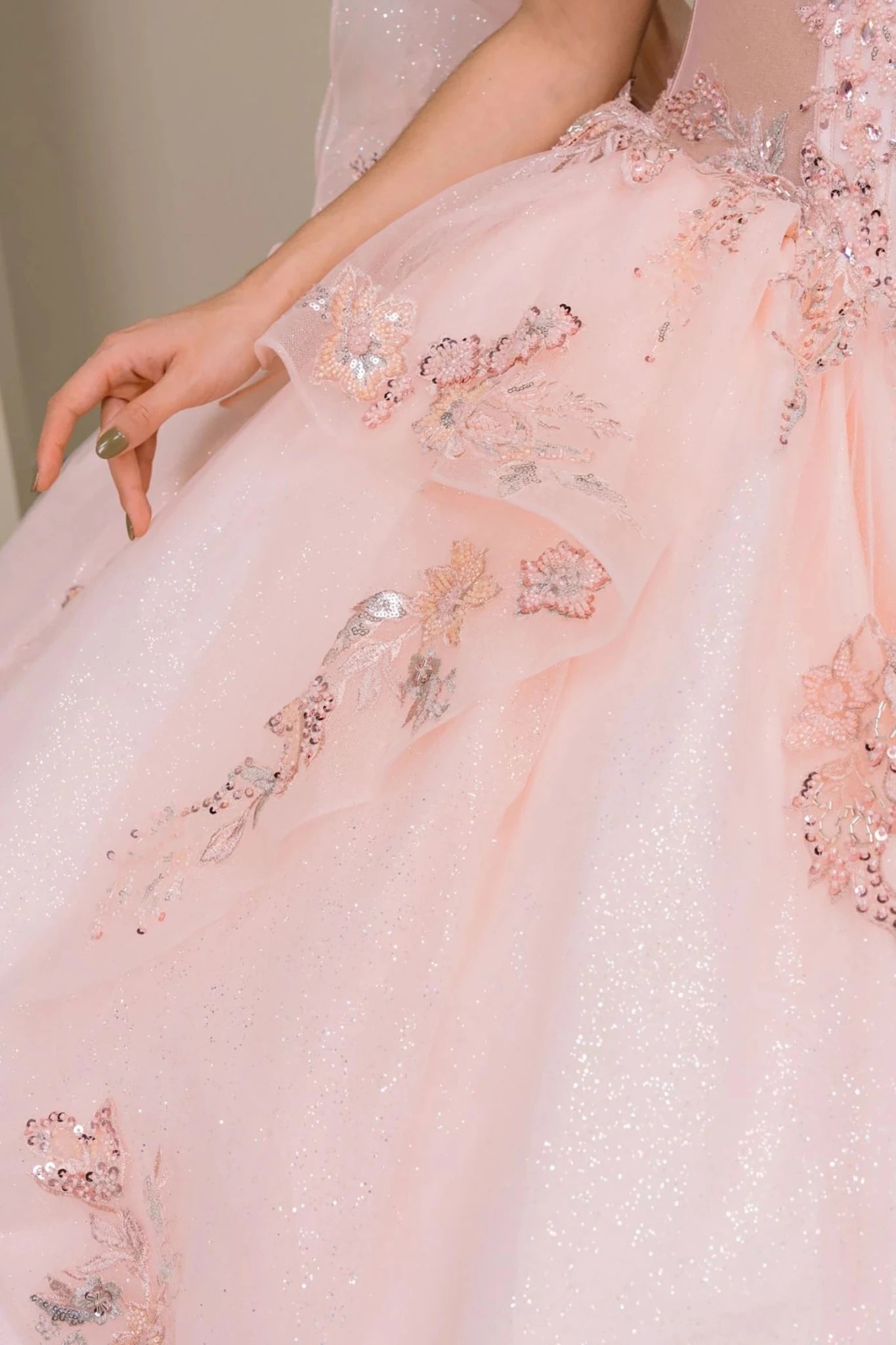 Close-up of blush quinceañera dress lower skirt with glitter tulle layers, floral appliqué accents, and flowing train