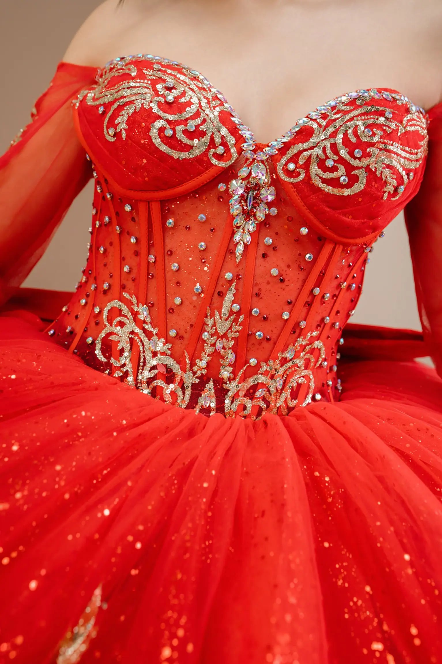 Bodice close-up of a woman wearing red quinceañera dress showing intricate gold embroidery, sequins, and beadwork details.