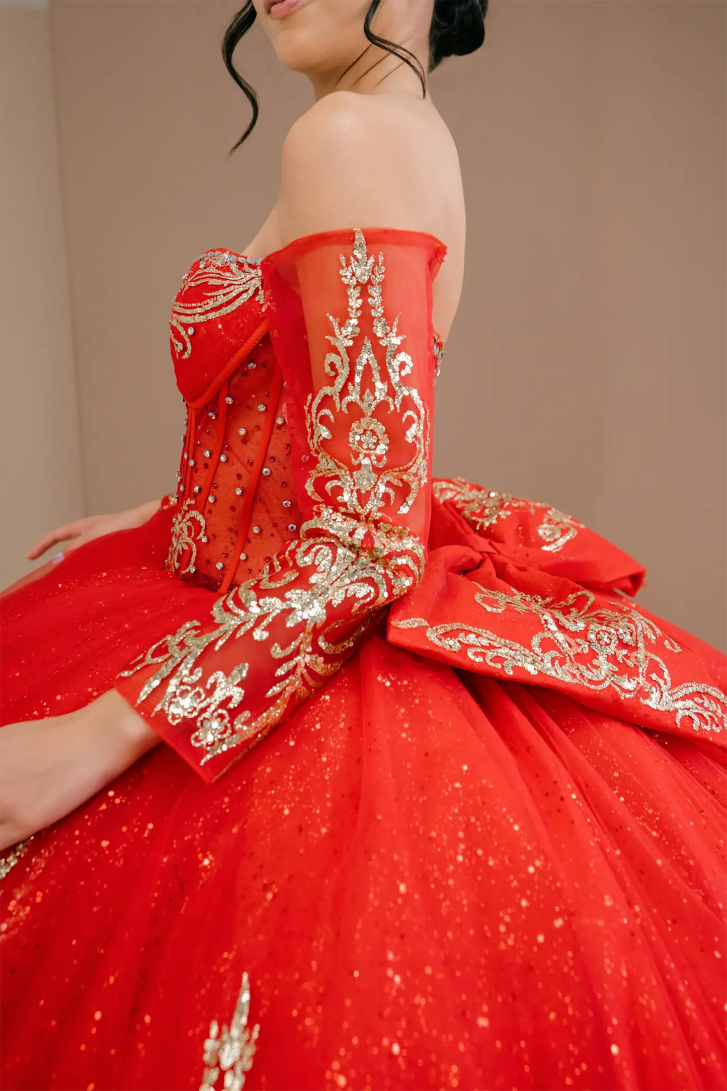 Side close-up view of a woman wearing red quinceañera dress highlighting glitter tulle layers, embroidered bodice, and corset silhouette.