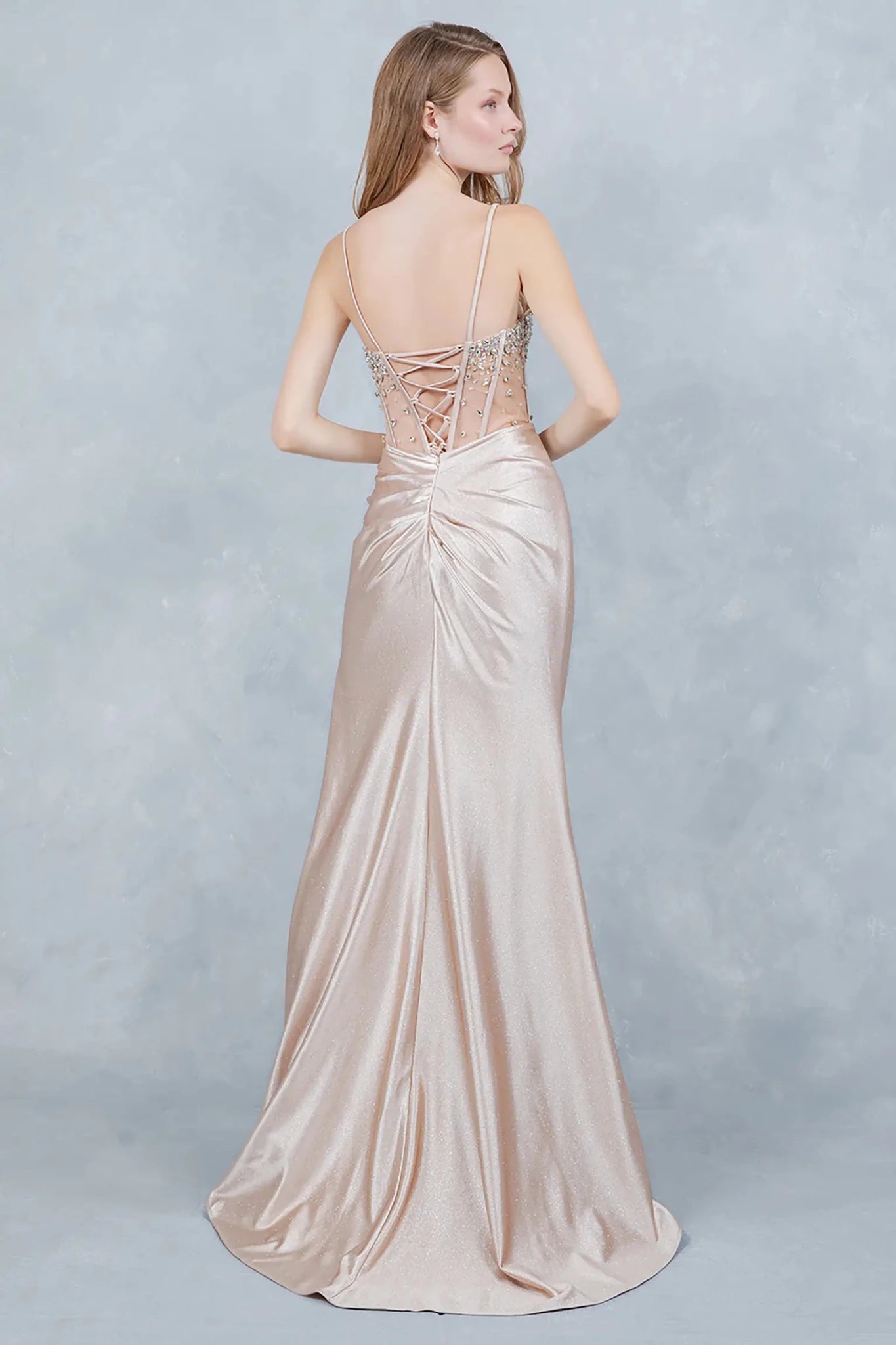 A full-length front view of a woman wearing a champagne glitter prom dress accented with a lace-up corset.